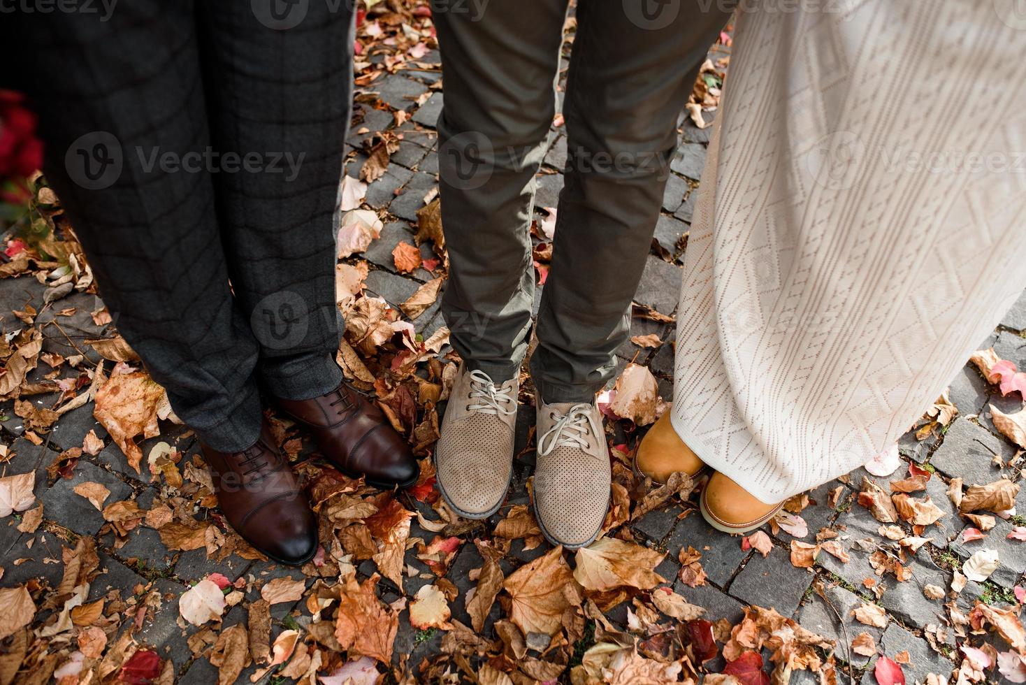 fötterna på bruden och brudgummen, såväl som deras son på bakgrunden av höstlöv foto