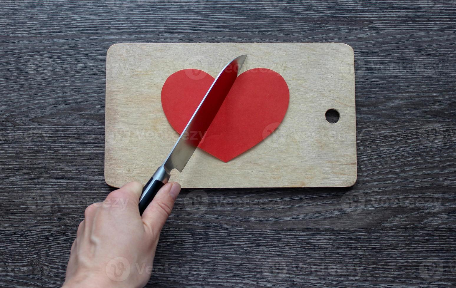 hand med en kniv skär ett pappershjärta på en skärbräda foto