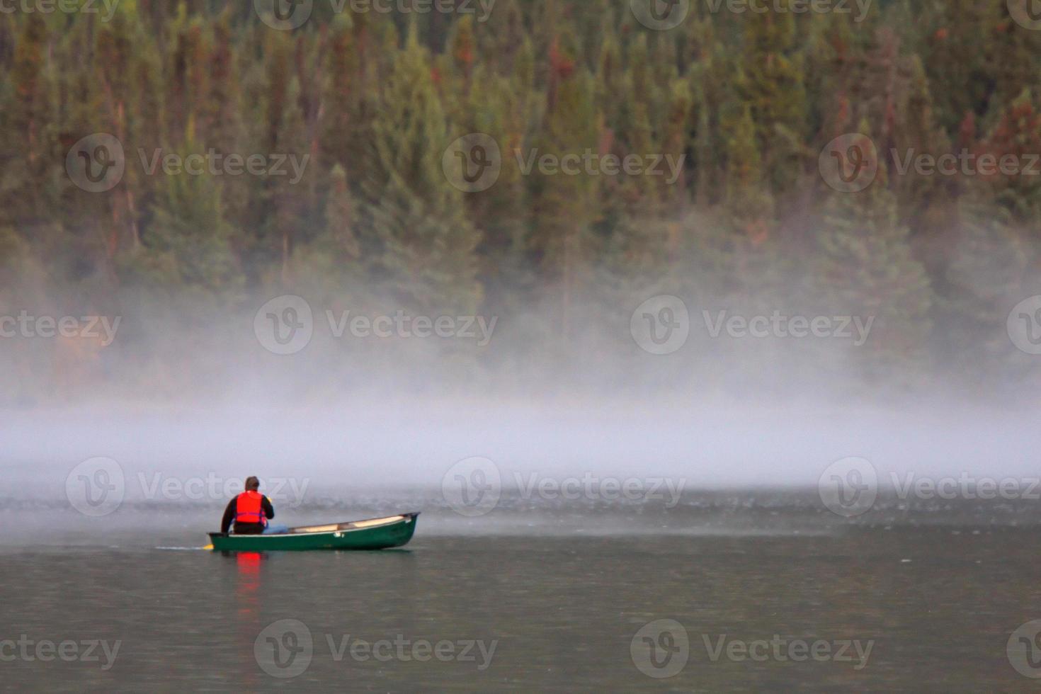 man i kanot nära morgondimma på sjön foto
