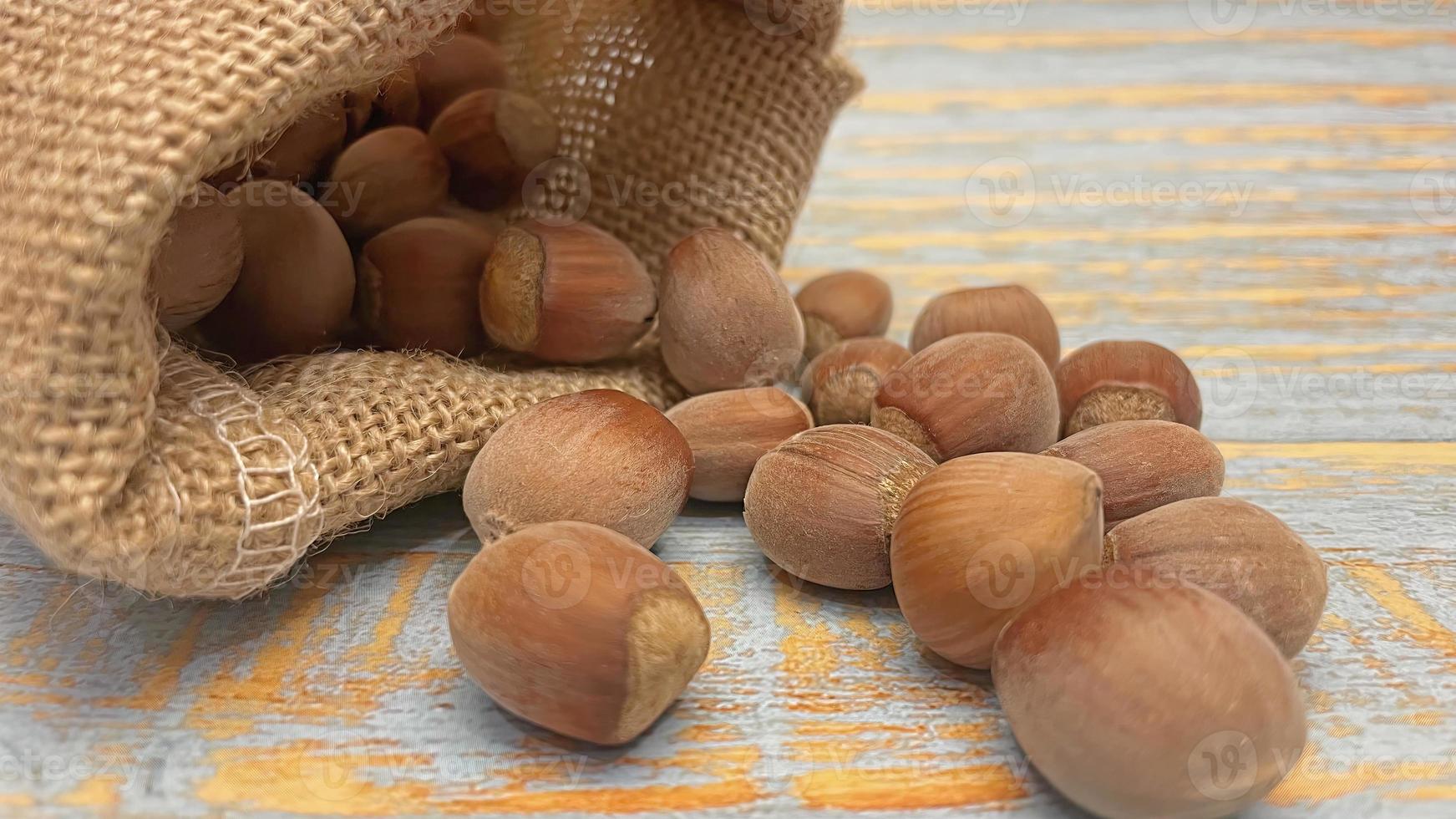 skalade hasselnötter i liten flätad säck på trä bakgrund foto