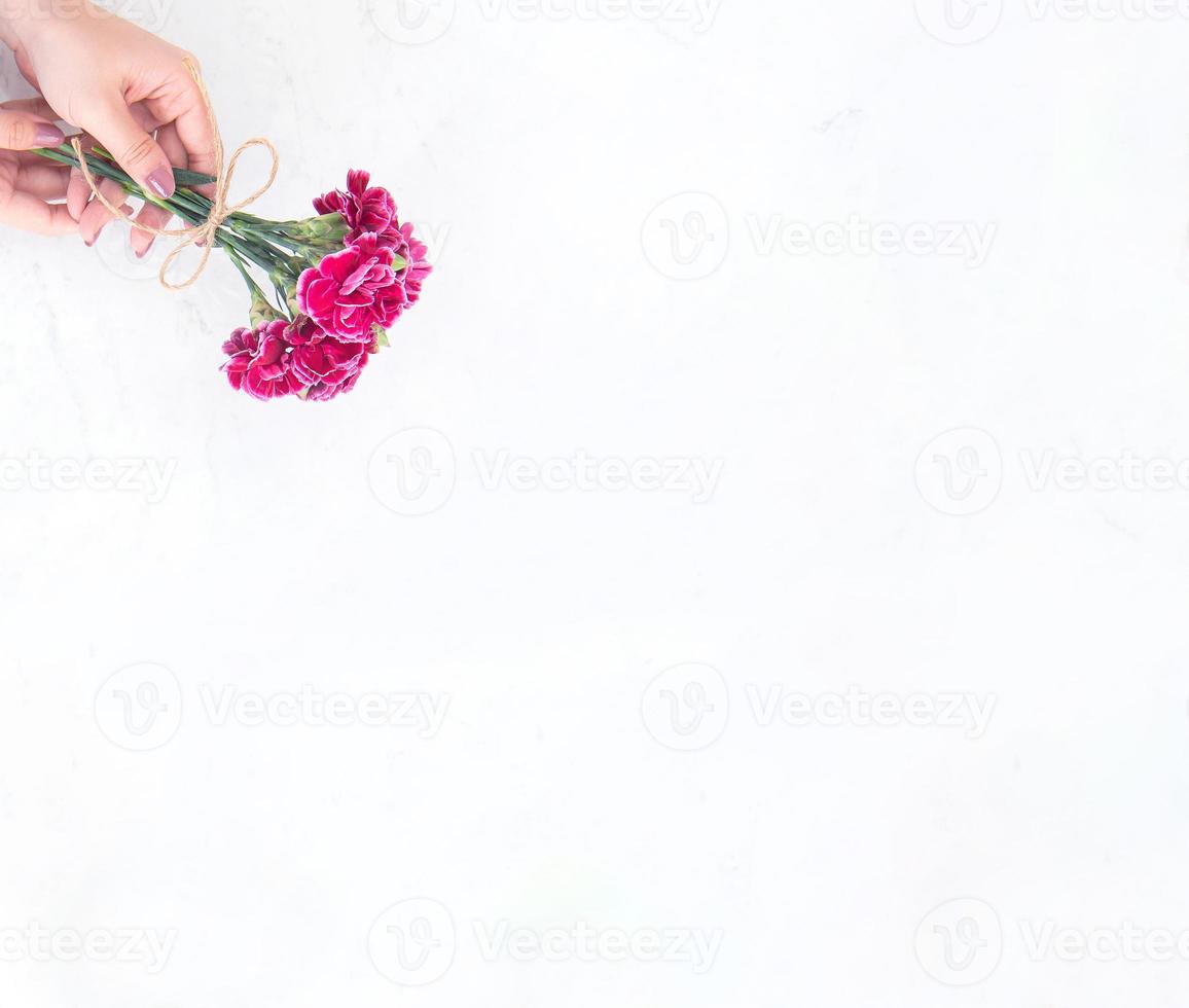 maj mors dag idékonceptfotografering - vackra blommande nejlikor bundna av repbåge som håller i kvinnans hand isolerad på ljust modernt bord, kopieringsutrymme, platt läggning, ovanifrån foto