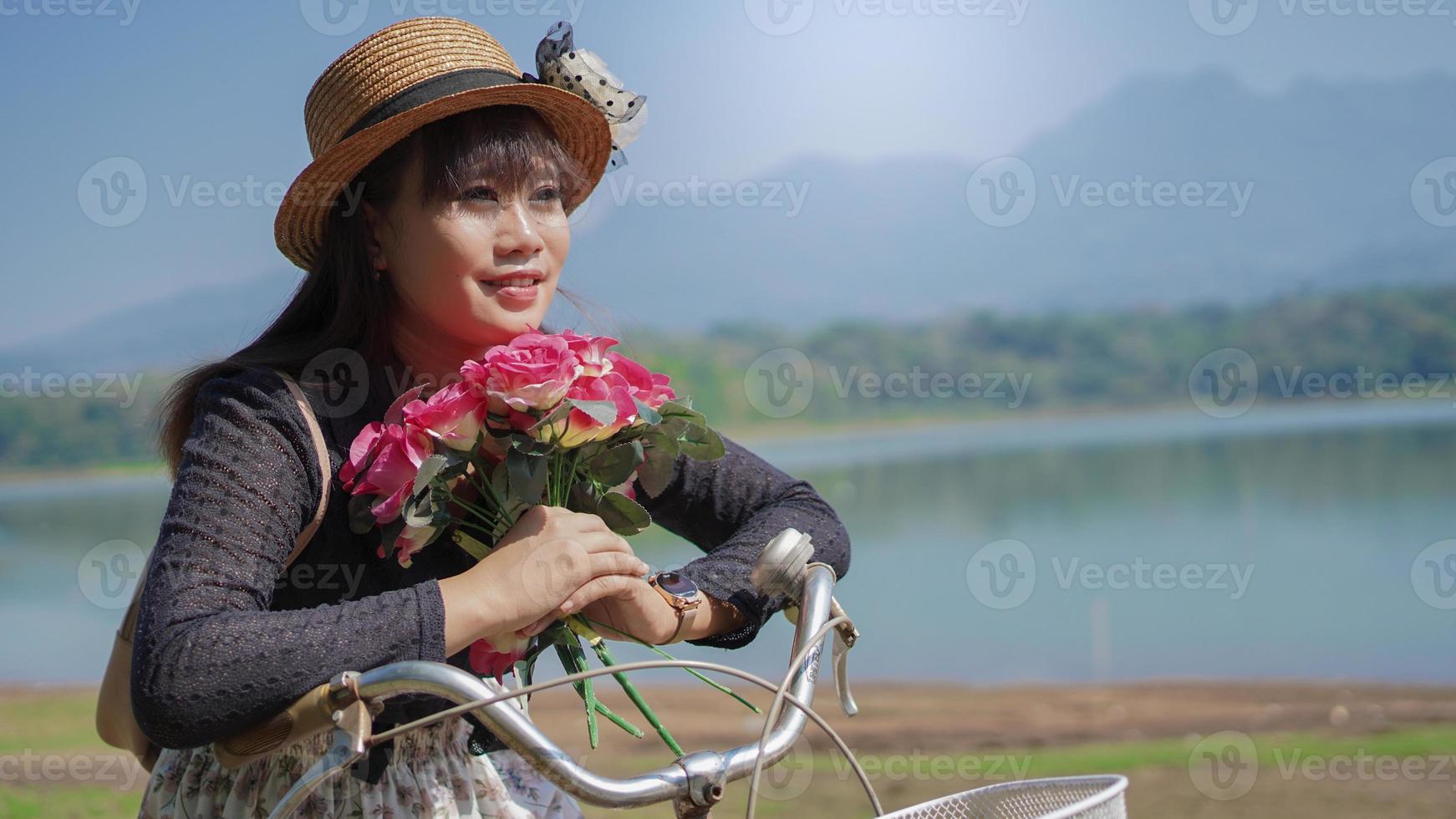 ung asiatisk kvinna njuter av att cykla medan hon stannar med blommor i parken foto