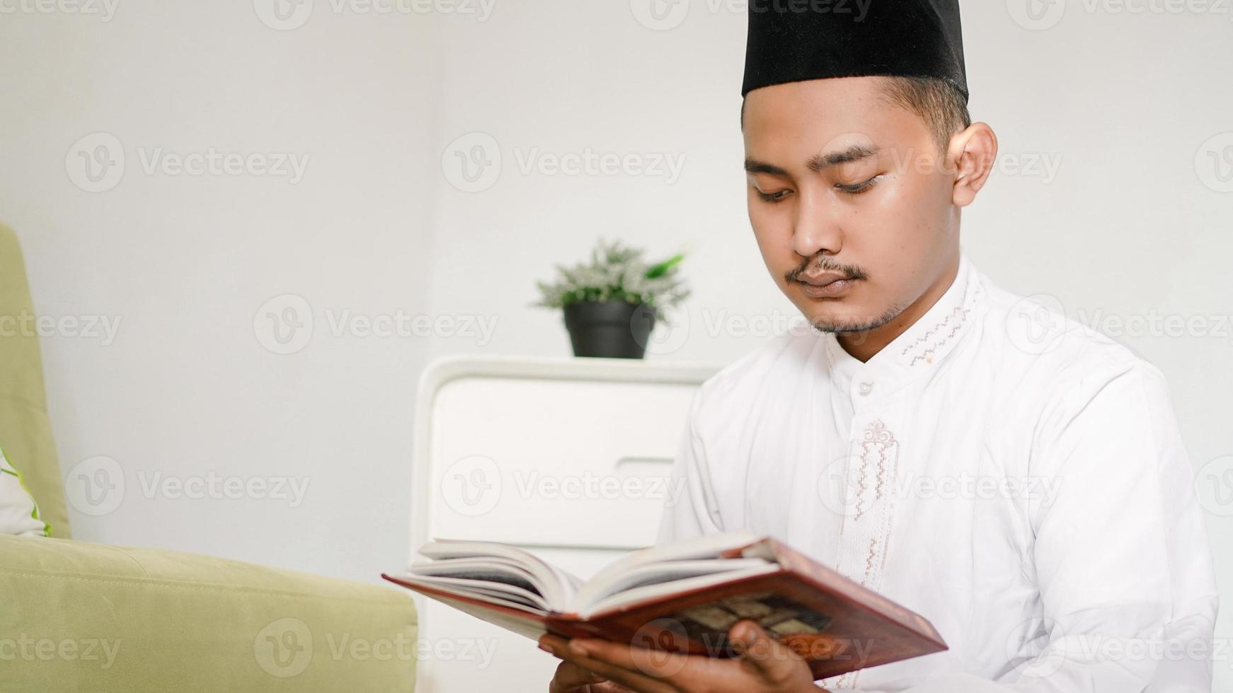 porträtt av asiatisk muslimsk man som läser den heliga koranen hemma foto