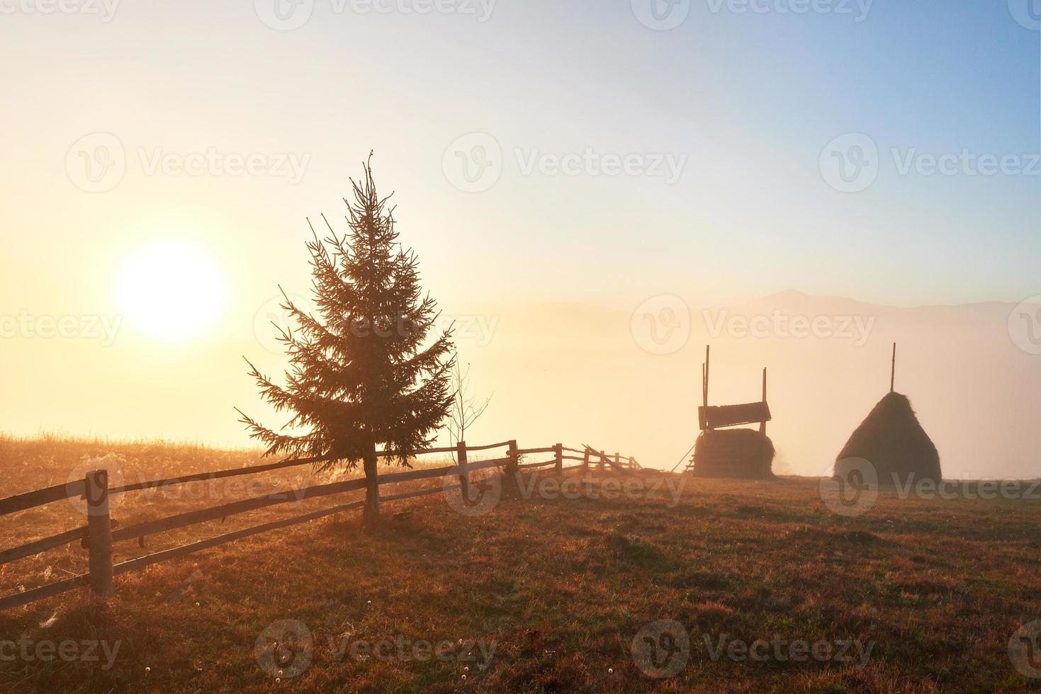 fantastiskt bergslandskap med dimma och en höstack på hösten foto