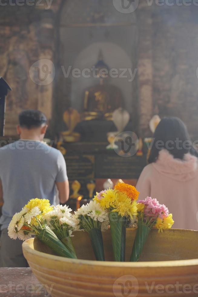 par människor ber till buddha i traditionell thailand tempel religiös. bukett blommig i förgrunden. vacker buddhism kultur respekt livsstil. lycklig familj brud och brudgum. foto