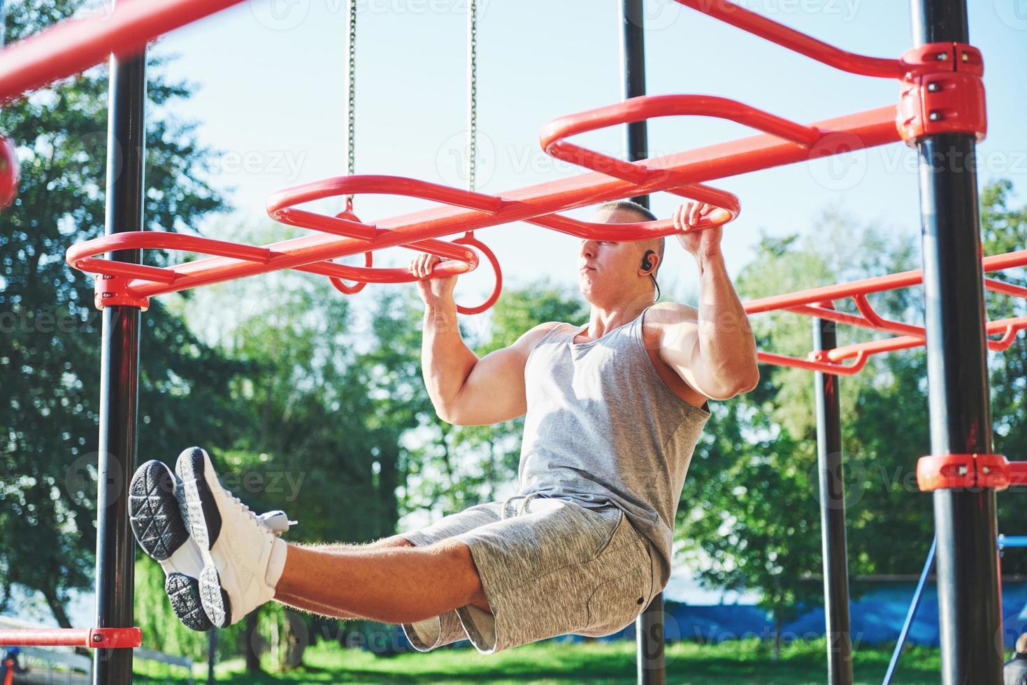 muskulös man med vacker överkropp som tränar på horisontella stänger på en suddig parkbakgrund. ung man gör pull-ups utomhus foto