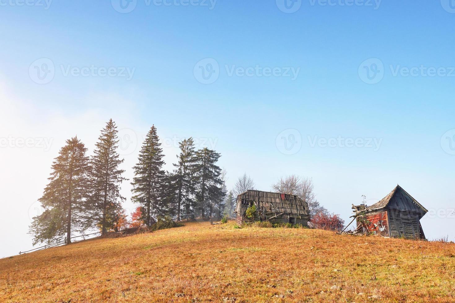 soluppgången ovanför den dimmiga dalen för höga berg med gamla trähus på en kulle i en bergsskog foto