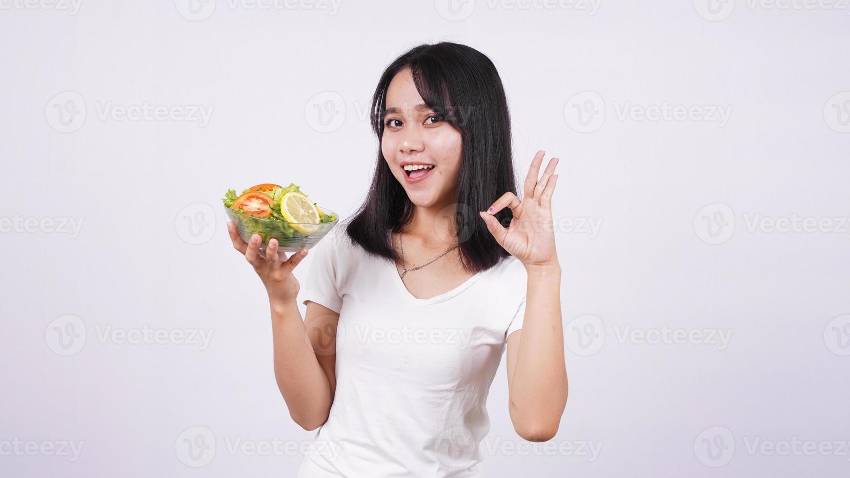 asiatiska kvinnor och okej finger på en skål med färska blandade grönsaker sallad med isolerade vit bakgrund foto