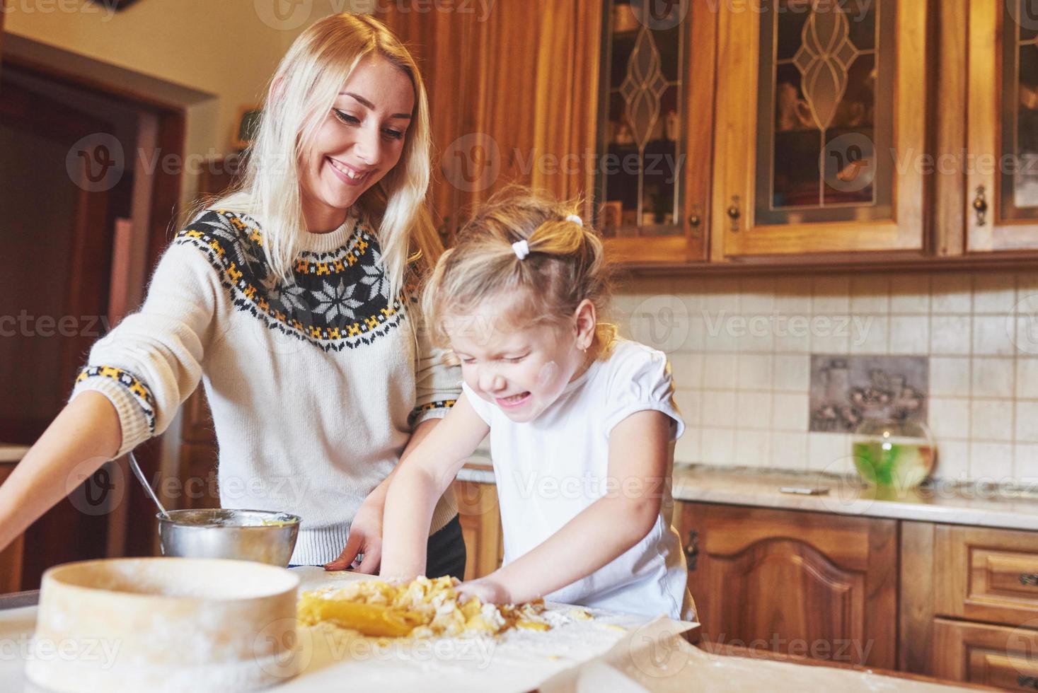 glad leende mamma i köket bakar kakor med sin dotter. foto