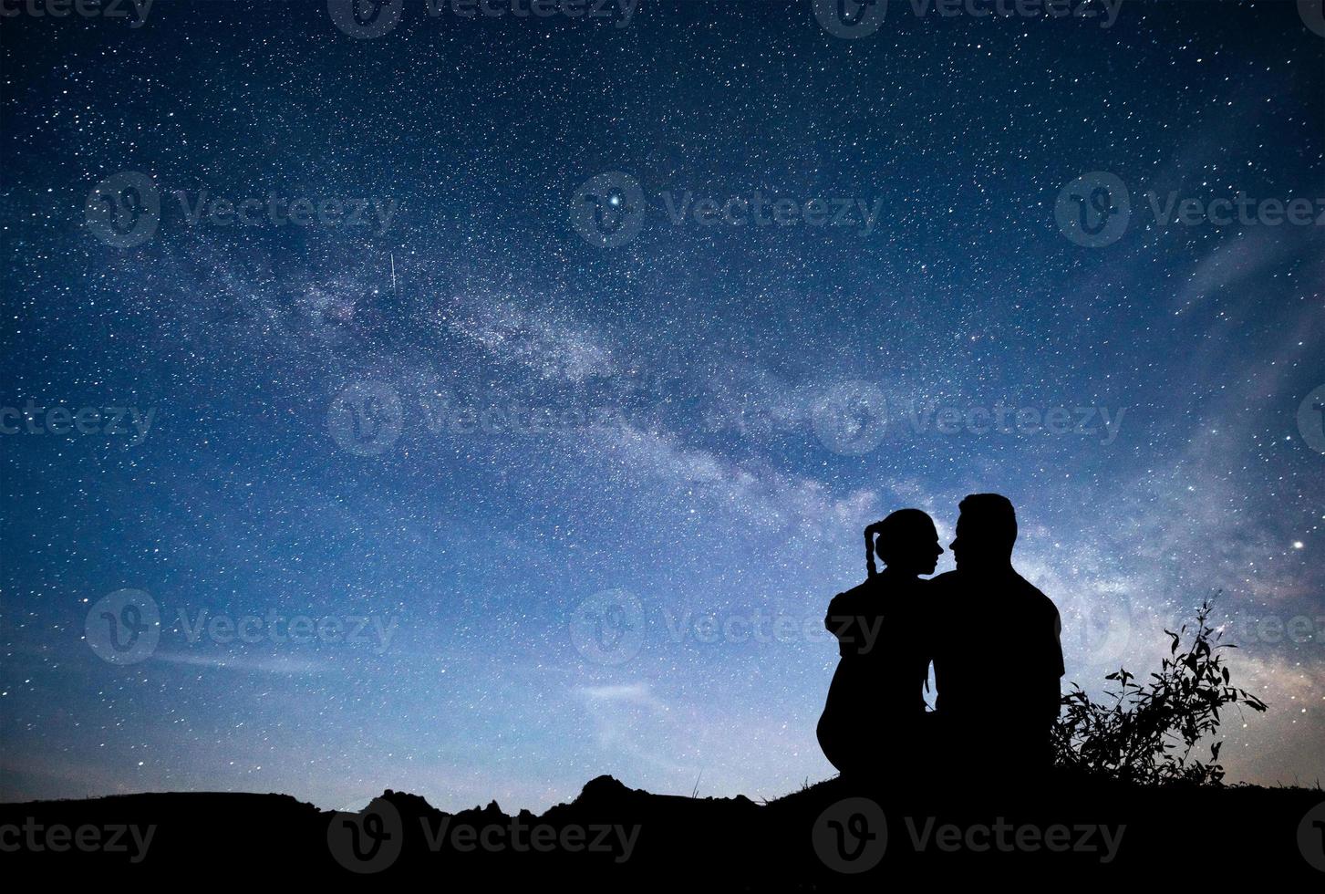 Vintergatan med siluett av människor. landskap med nattstjärnhimmel. stående man och kvinna på berget med stjärnljus. kramar par mot lila Vintergatan. foto