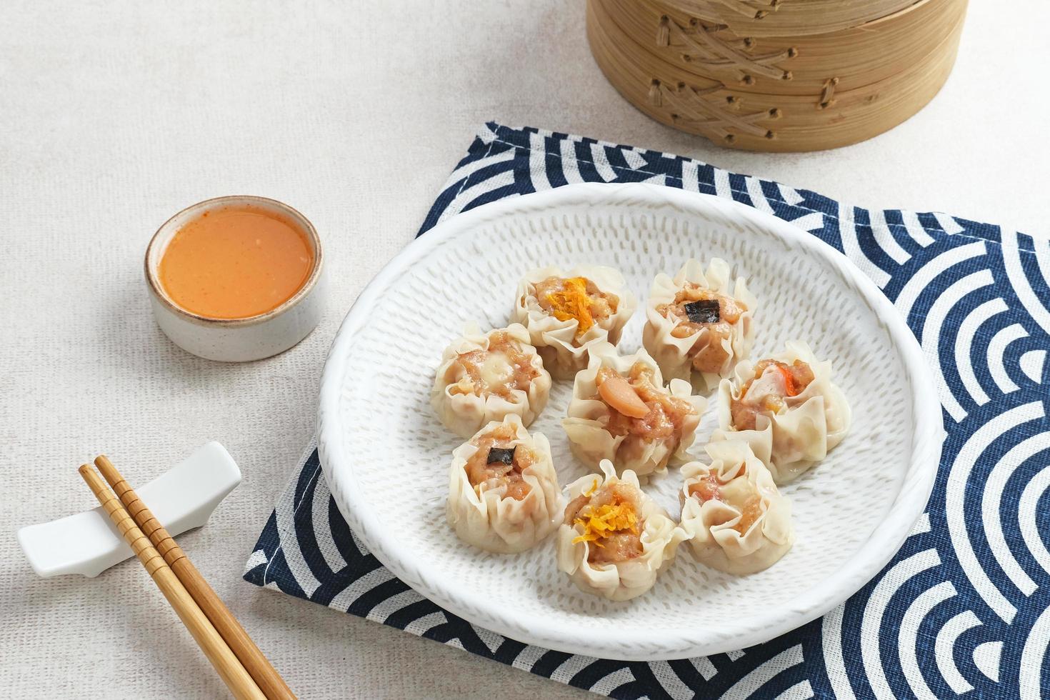 mini dim sum kinesiska dumplings serveras på vit tallrik, med sås och ätpinne. närbild. foto