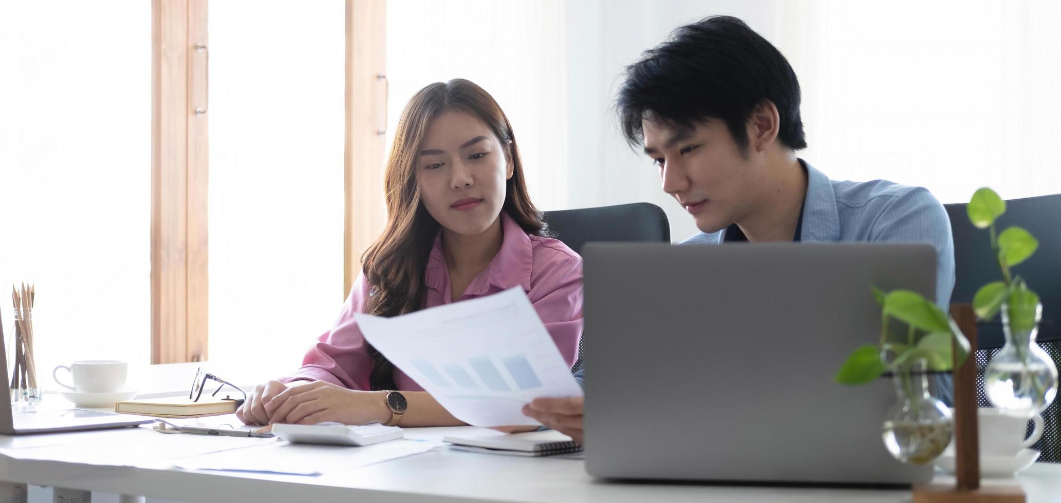 två glada asiatiska unga affärsmän som arbetar tillsammans med en surfplatta på ett modernt kontor. planerar att analysera den ekonomiska rapporten, affärsplansinvesteringar, finansanalyskoncept foto