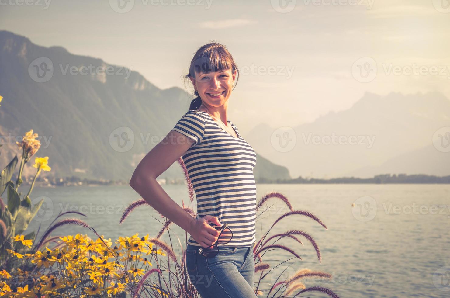 ung vacker flicka med randig skjorta och jeans poserar och leende på vallen av sjön Leman Geneva foto
