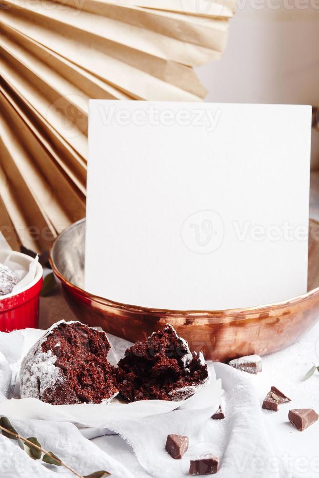 chokladmuffins i röda koppar. mockup vitt papper copyspace. liten glaserad keramisk ramekin med bruna kakor på en grå och vit bakgrund. foto