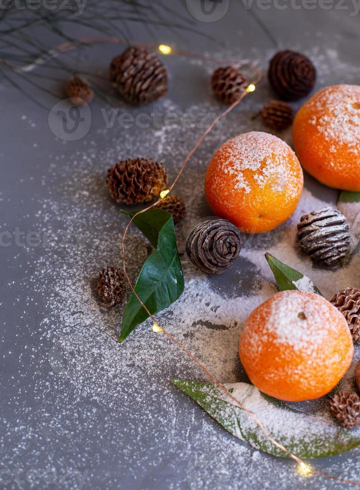 orange mandariner på grå bakgrund i nyårsdekor med bruna kottar och gröna blad. juldekoration med mandariner. utsökt söt clementin. foto