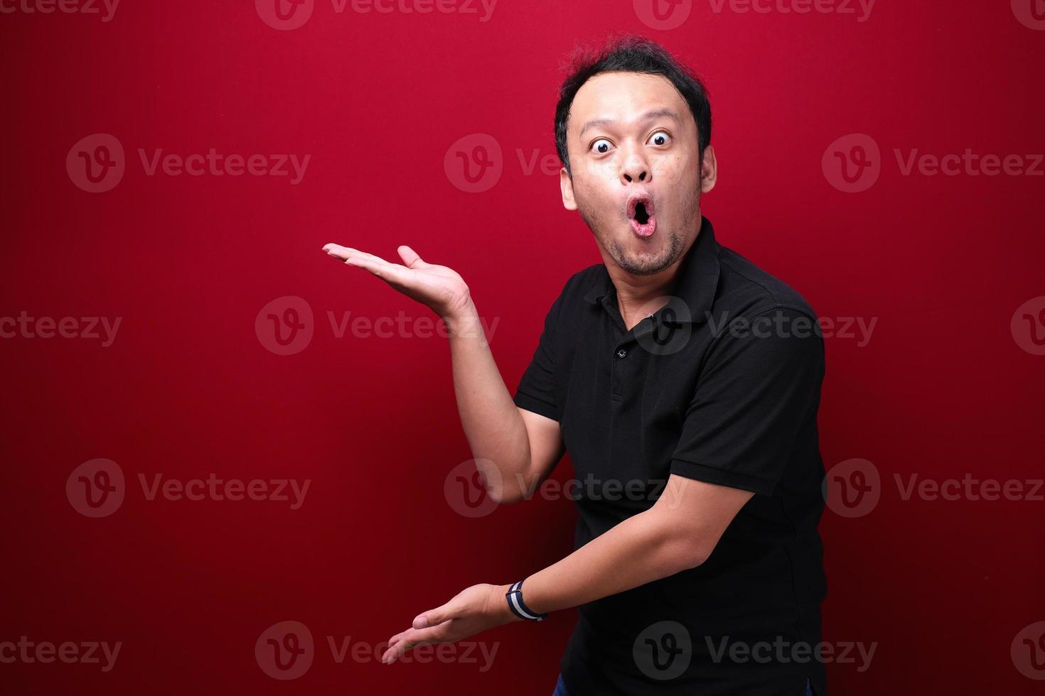 ung asiatisk man är förvånad och skriker wow med att peka höger med handen isolerad på röd bakgrund. foto