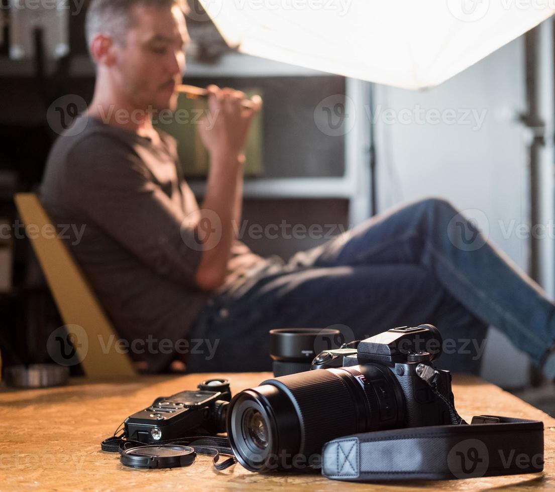 kamera och utrustning på bordet i studion i bakgrunden av den sittande fotografen foto