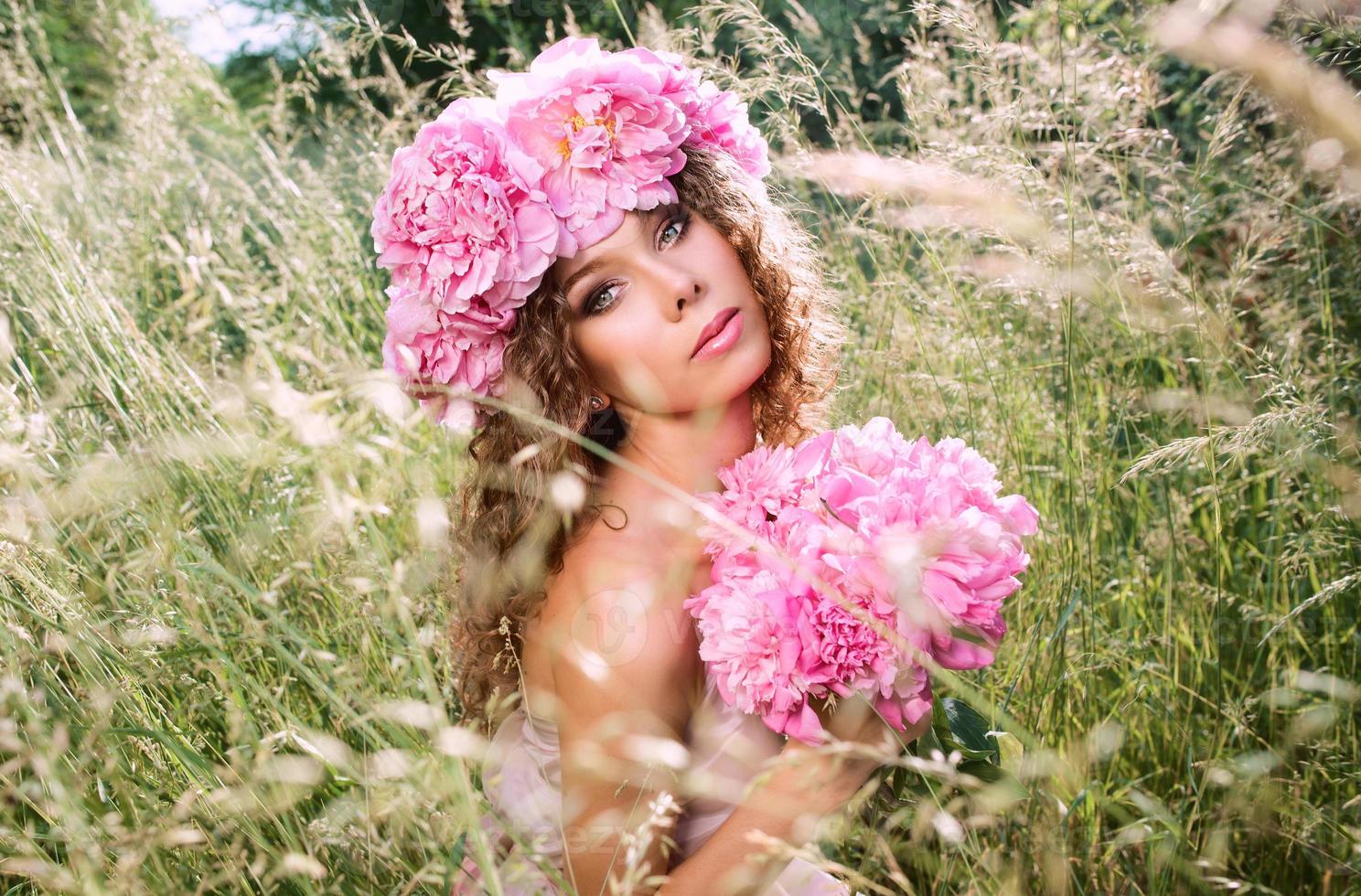 kaukasisk vacker kvinna med en krans av rosa pioner på huvudet. våren, blomma, fairy koncept foto