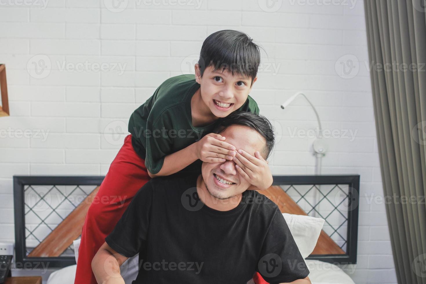 pojke stänger sin fars ögon för att göra överraskning hemma under fars dag foto