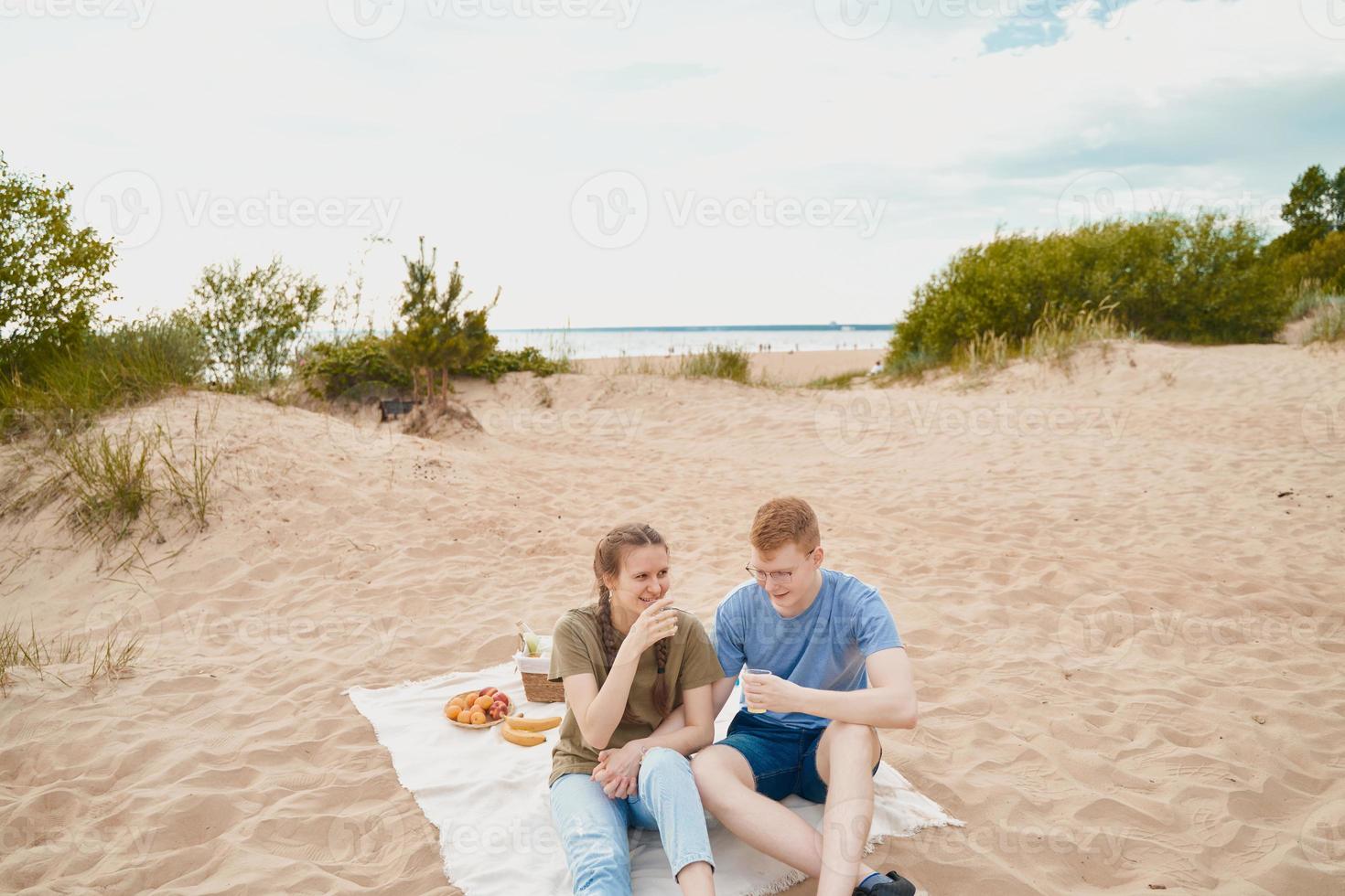 picknick på stranden med mat och dryck. ung pojke och flicka sitter på sand foto