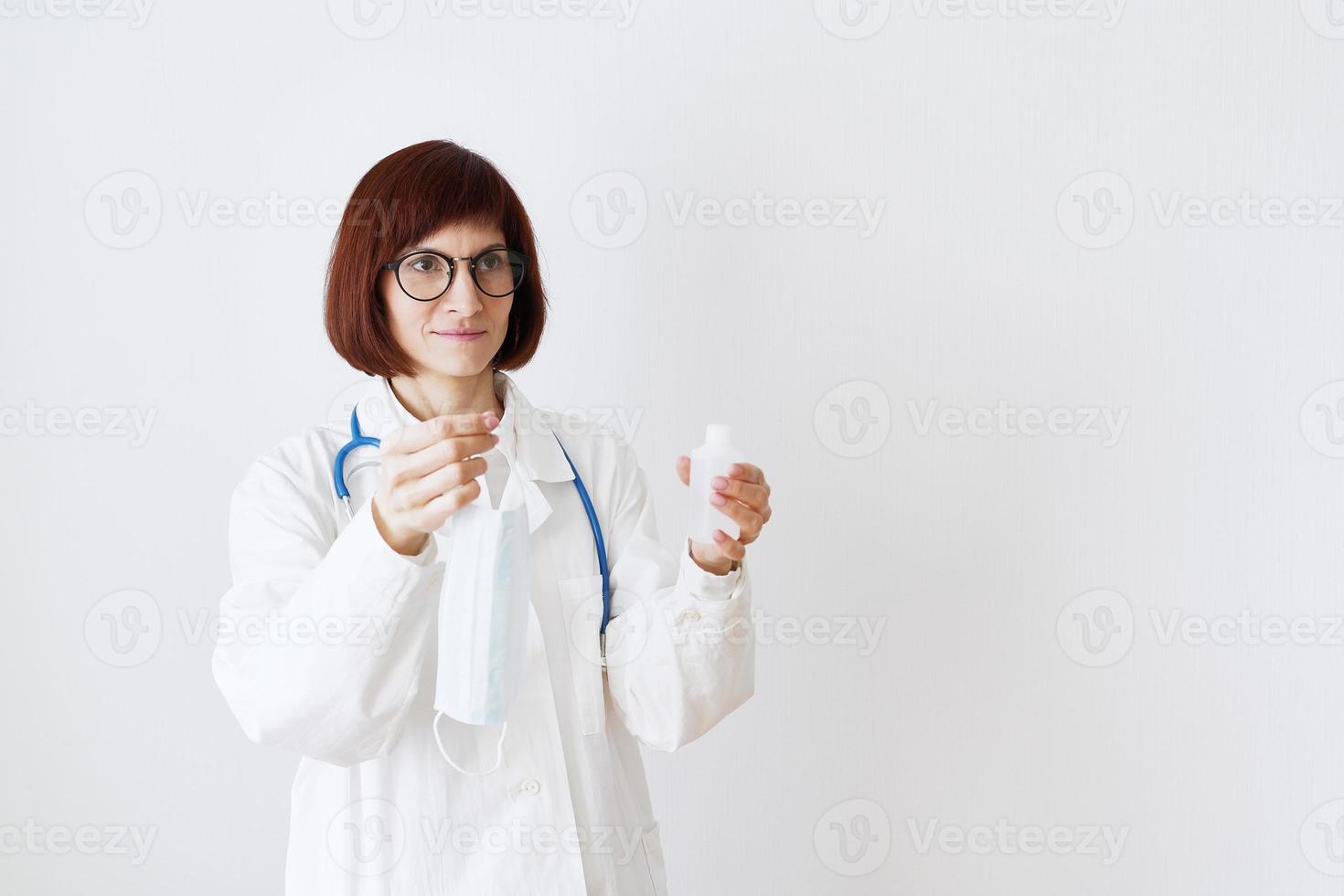 kvinnlig läkare i medicinsk mask och uniform erbjuder mask och desinfektionsmedel i flaska foto
