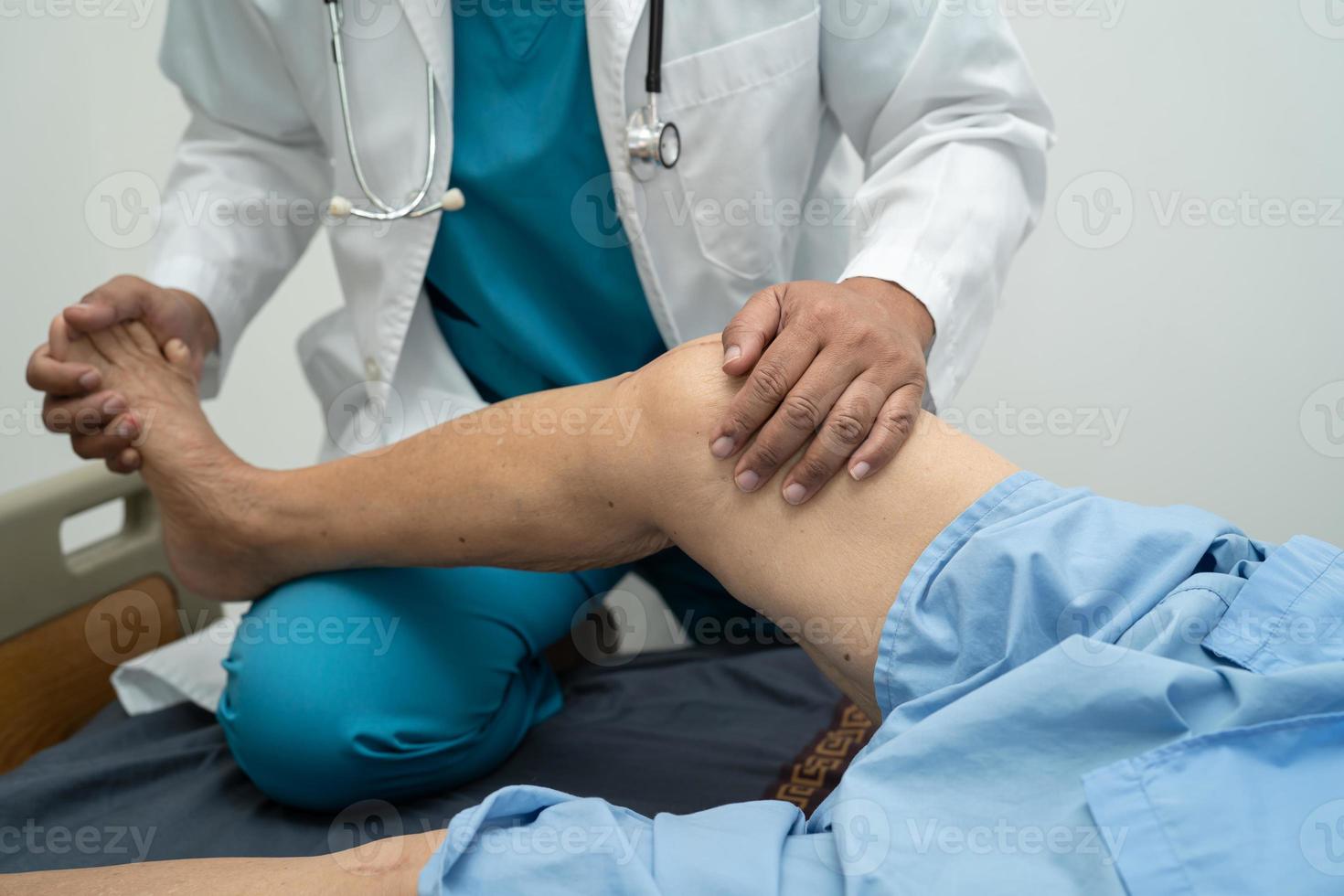 asiatisk läkare fysioterapeut undersöker, masserar och behandlar knä och ben hos senior patient på ortopedmedicinsk klinik sjuksköterska sjukhus. foto
