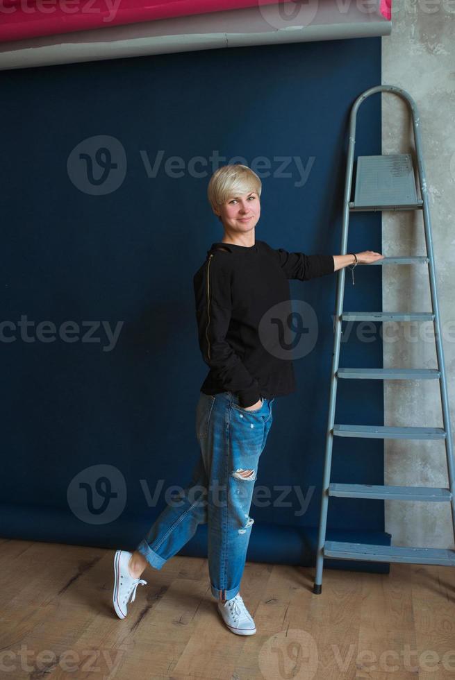 ung blond modern kvinna i svart tröja och jeans som står nära stege och planerar renovering foto