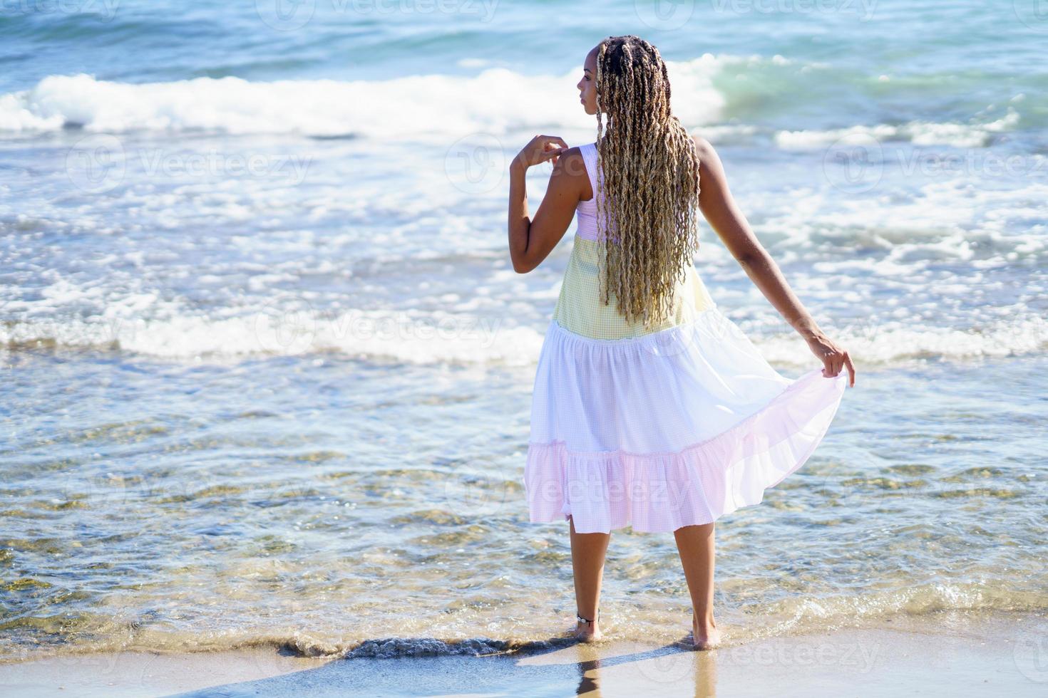 svart kvinna går längs stranden av stranden bär en vacker lång klänning. foto