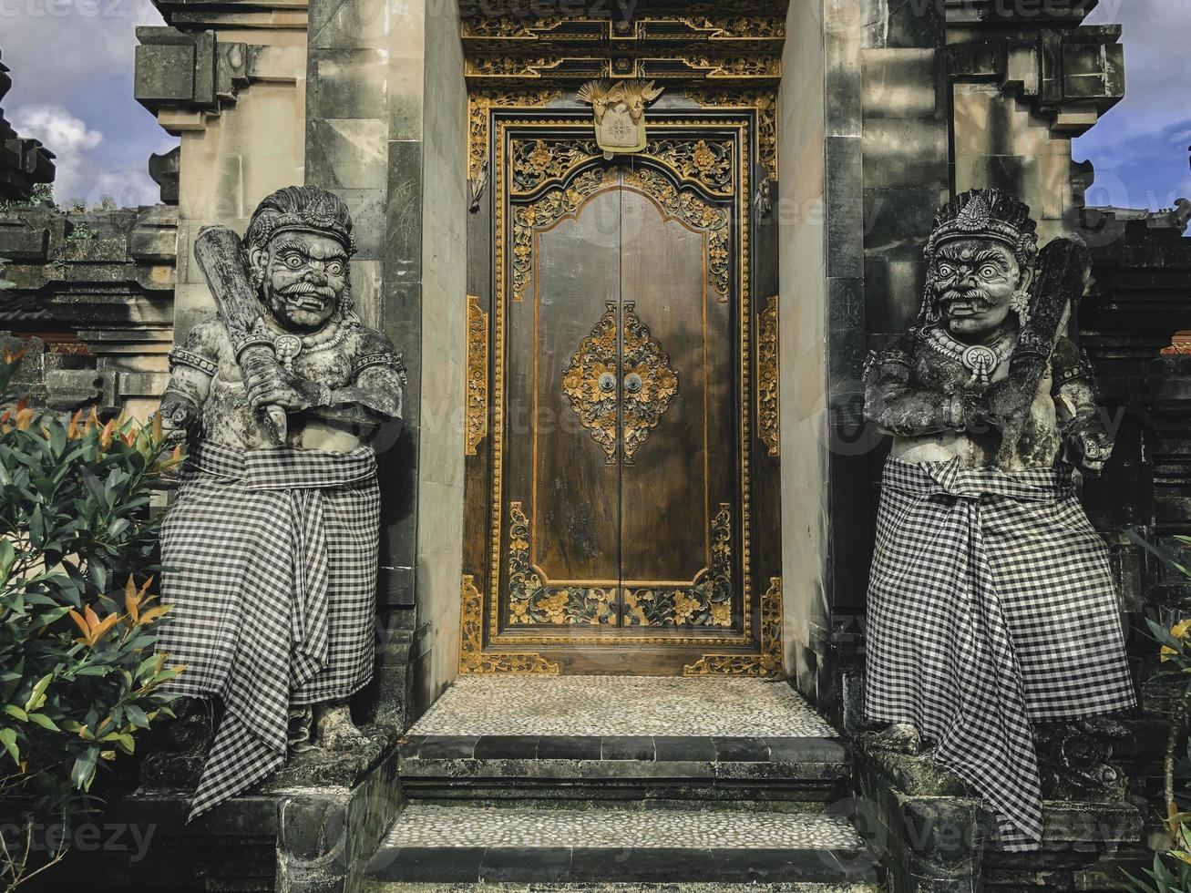 dörr eller grind för att komma in i traditionell balinesisk trädgårdsarkitektur. indonesisk träport bevakad av stenstatyer. foto