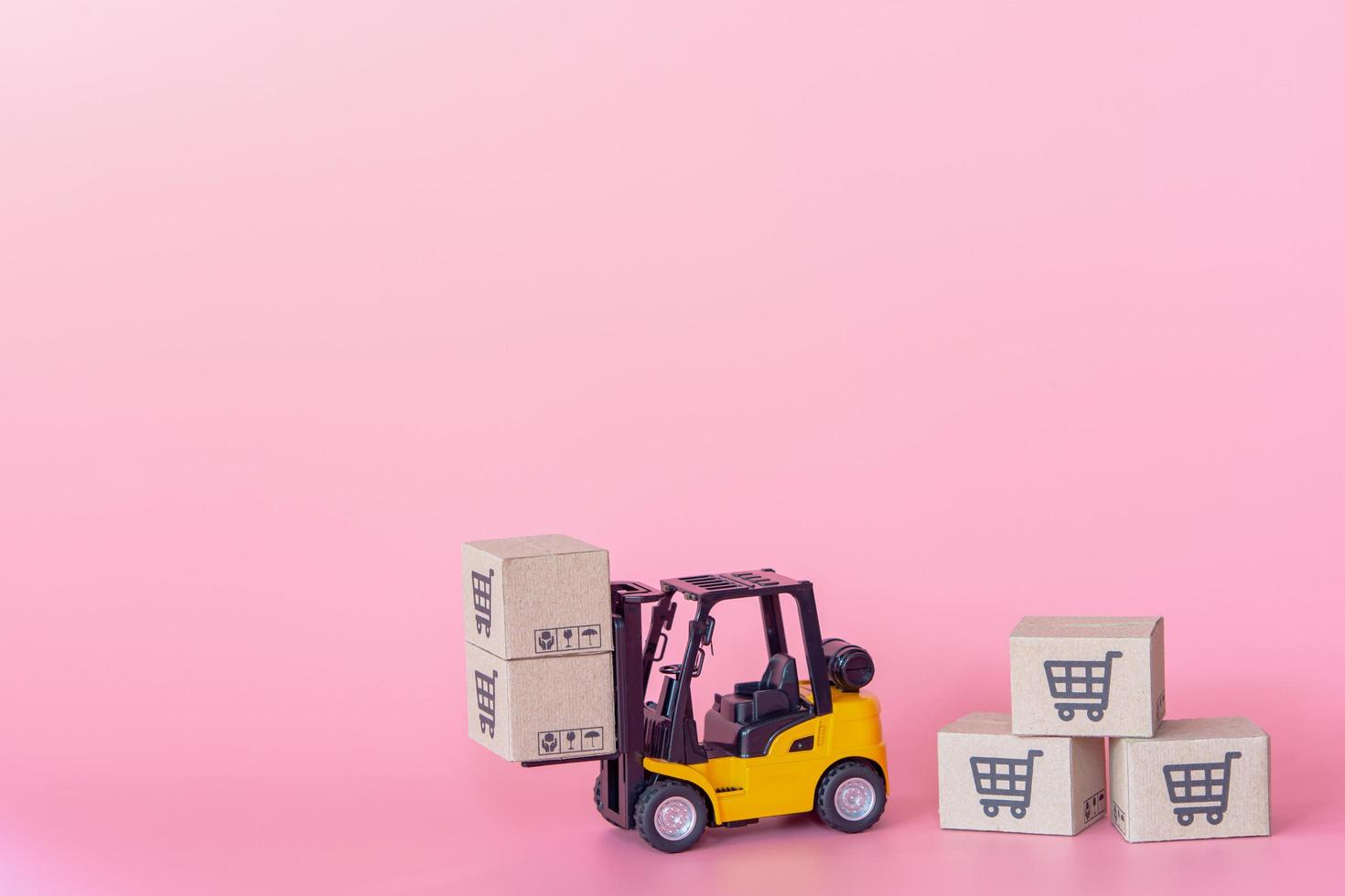 logistik och leveransservice - gaffeltruckmodell och papperskartonger eller paket med en kundvagnslogotyp på rosa bakgrund. shoppingtjänst på webben och erbjuder hemleverans. foto