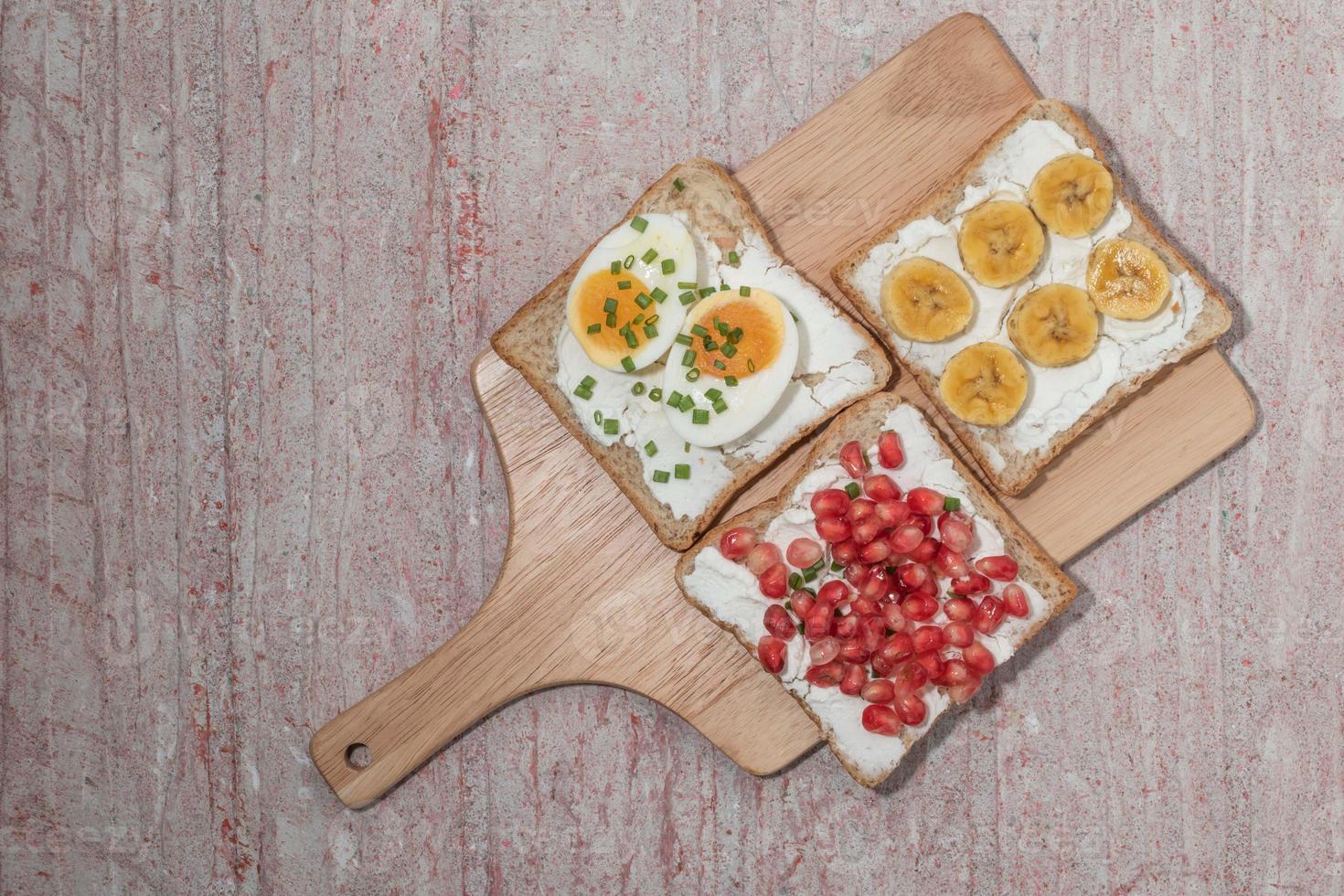 bröd har färskost och granatäpple kokt ägg banan på röd bakgrund. foto