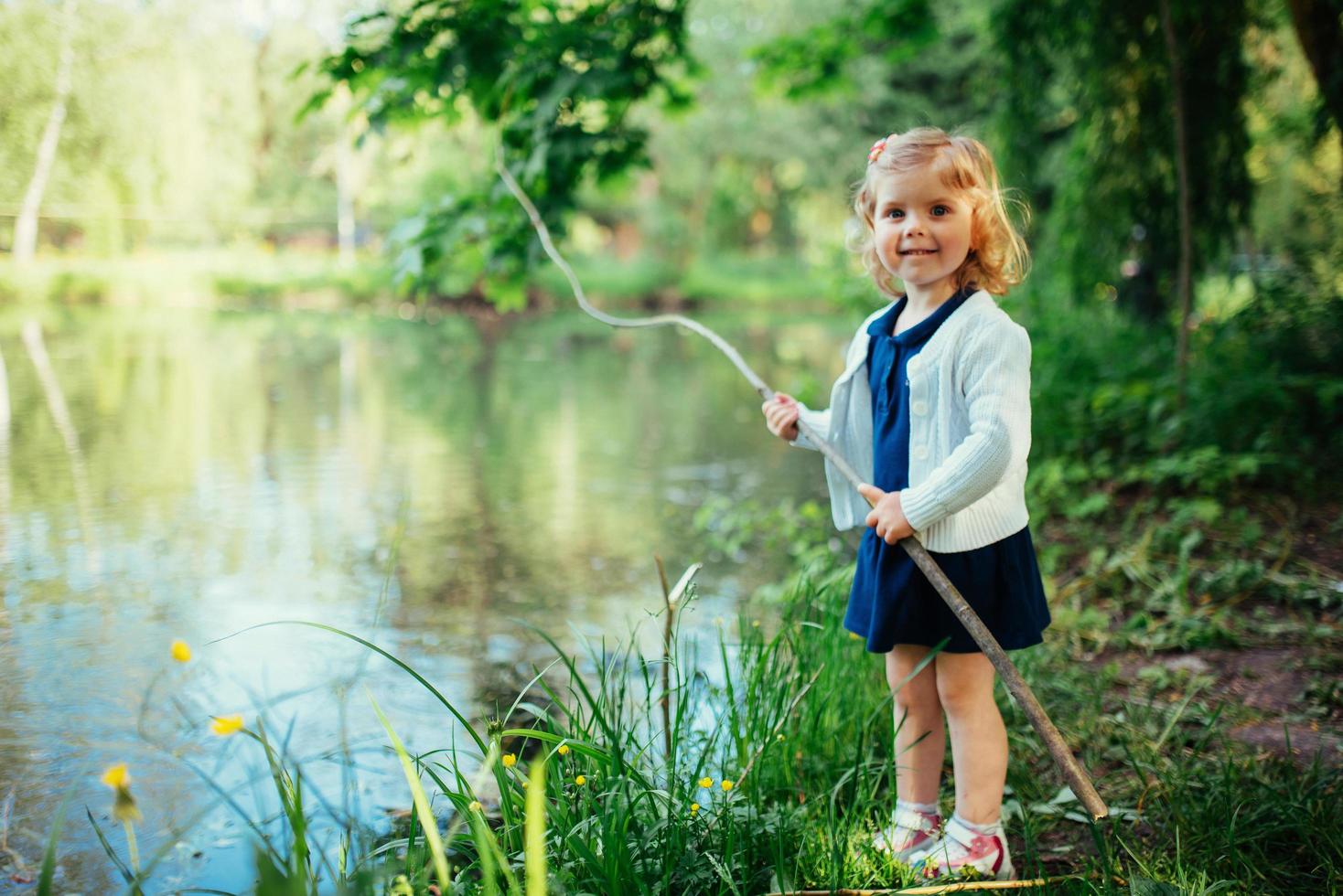 söt liten blond flicka är mot bakgrund av vatten och g foto