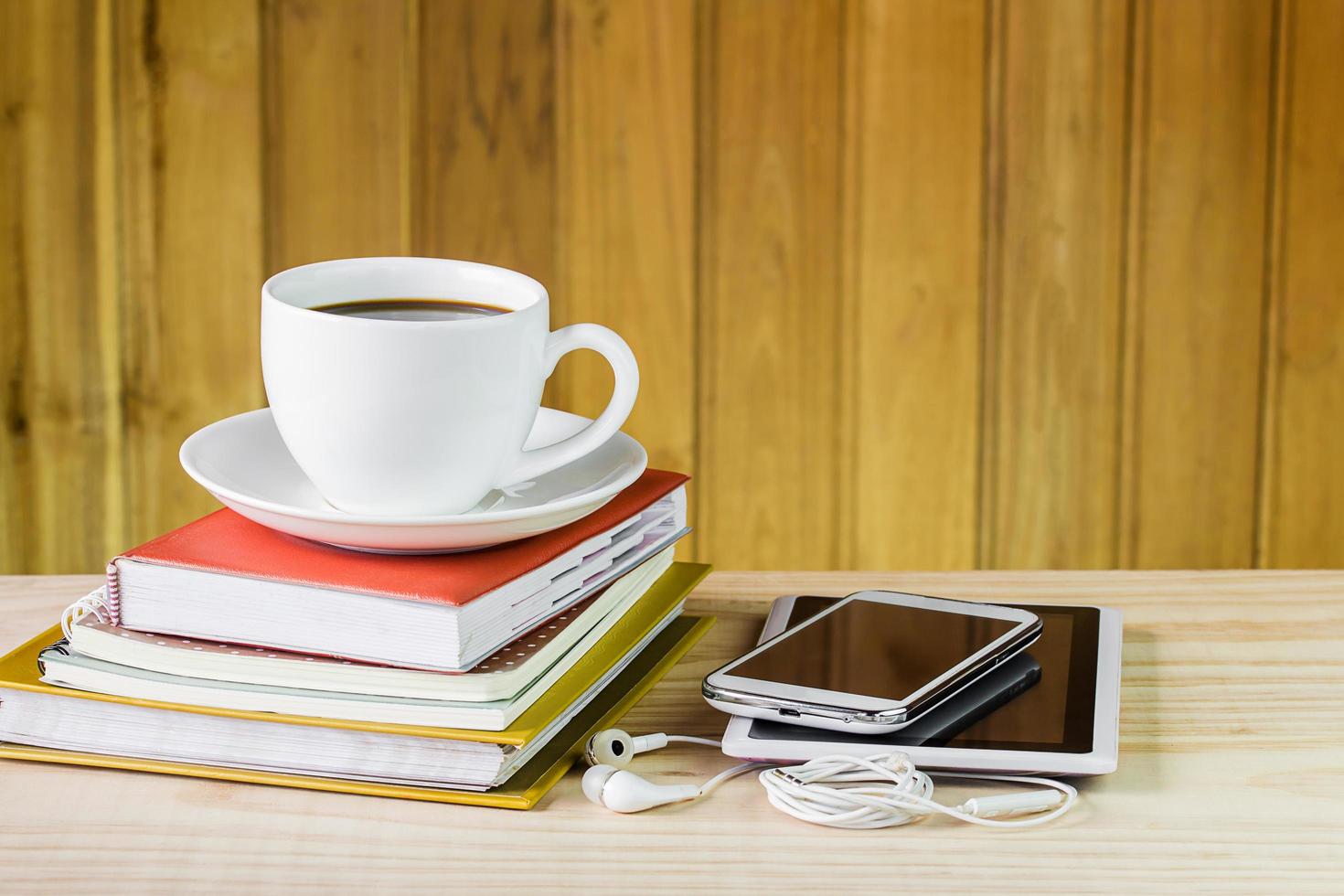 smart telefon, kaffekopp och hög med bok på träbord foto