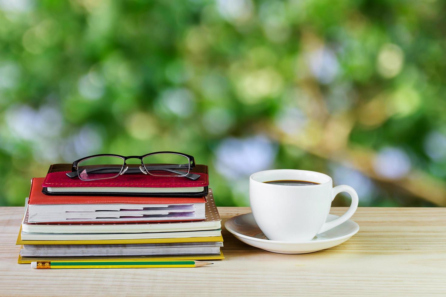 kaffekopp, glas och hög bok på träbord med oskärpa bakgrund foto