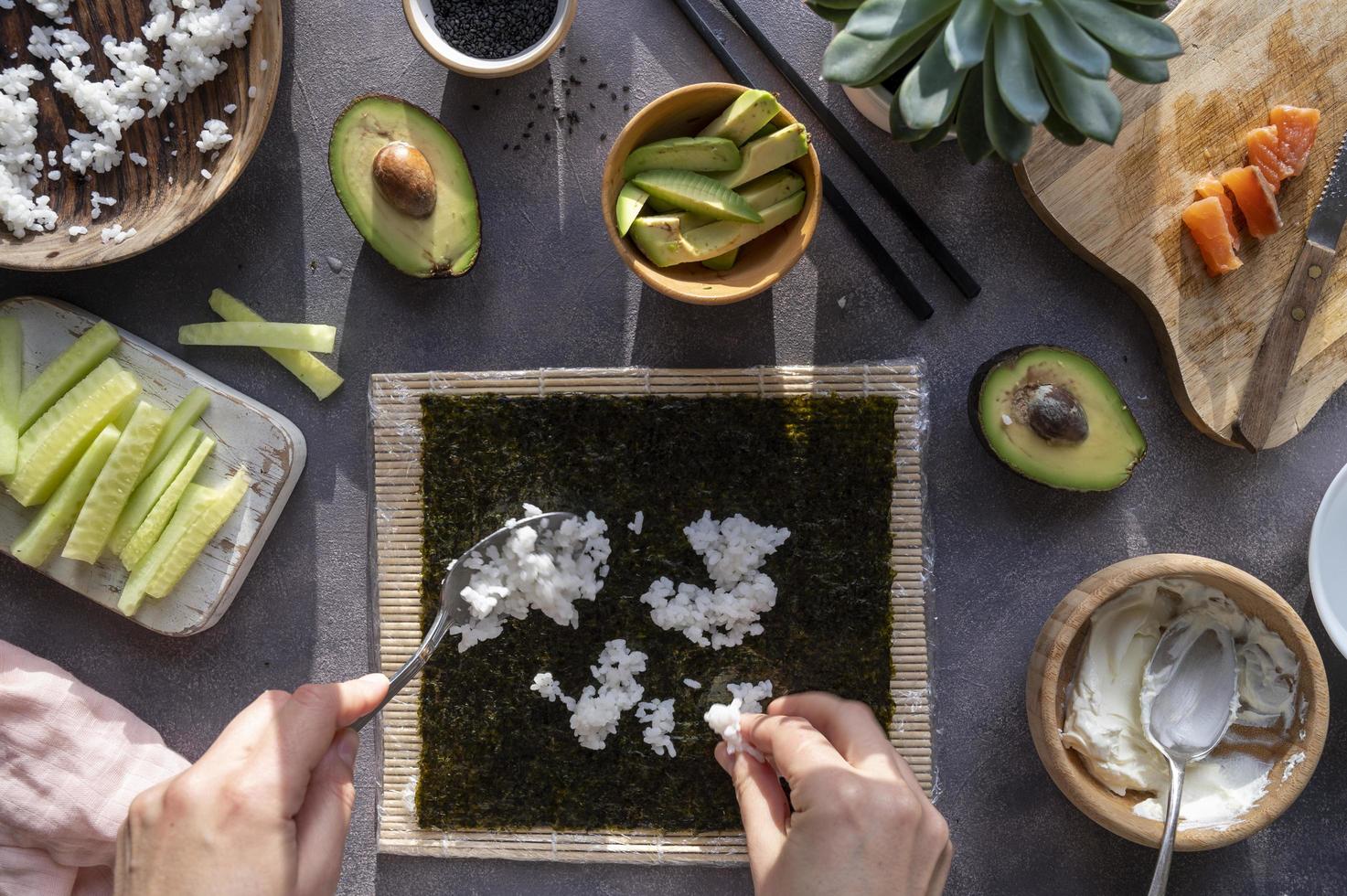 laga sushirullar hemma med lax, avokado och gurka. kvinnlig hand förbereder avokadosushi, steg för steg. foto