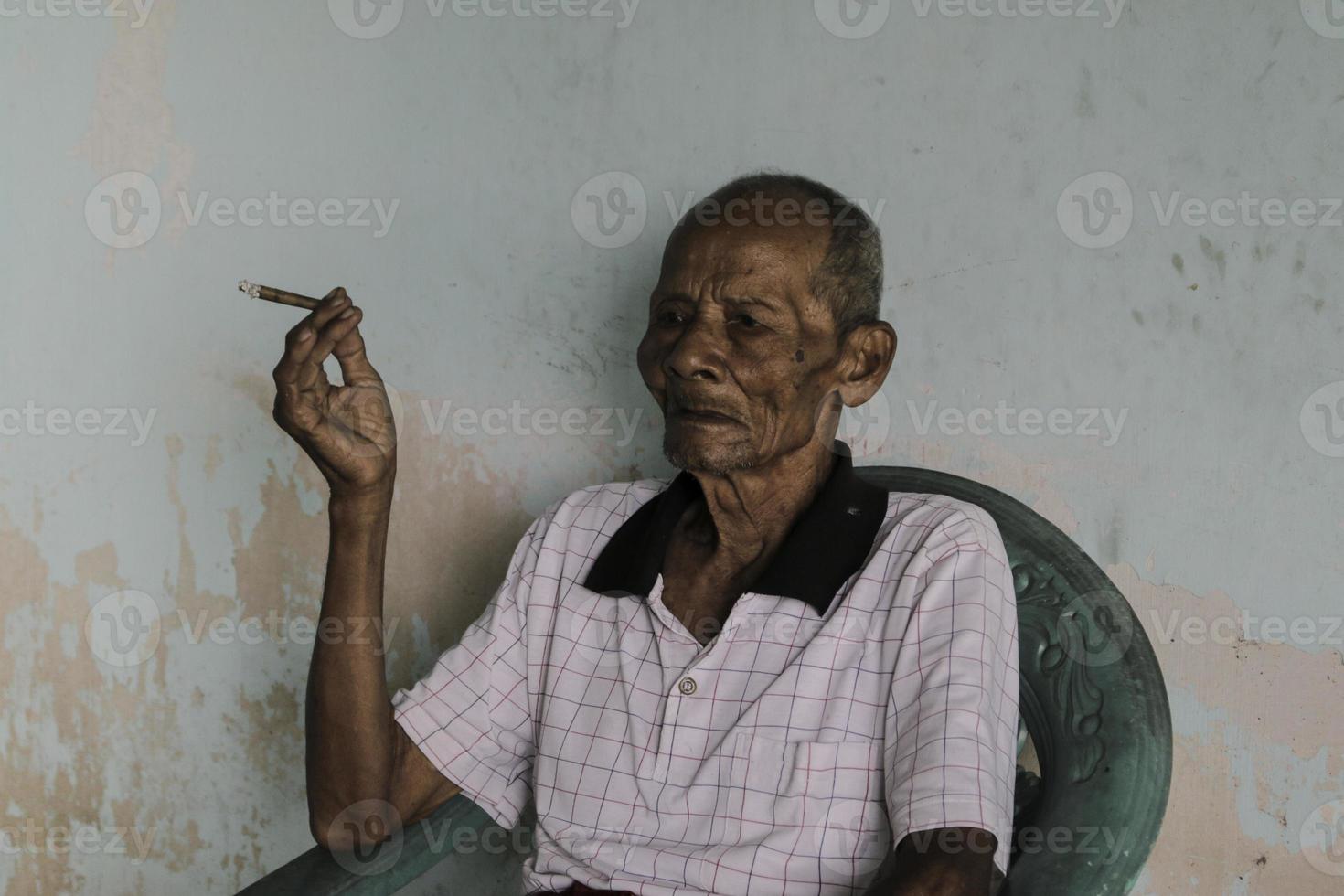 närbild porträtt av asiatisk javanesisk gubbe med en cigarett i handen foto