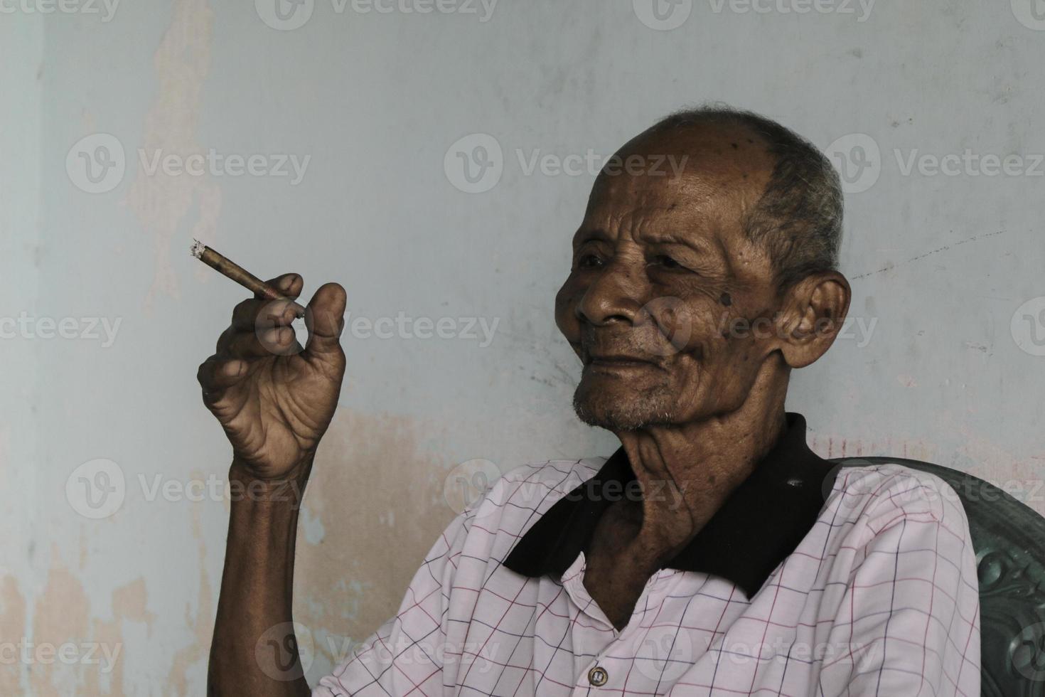 närbild porträtt av asiatisk javanesisk gubbe med en cigarett i handen foto