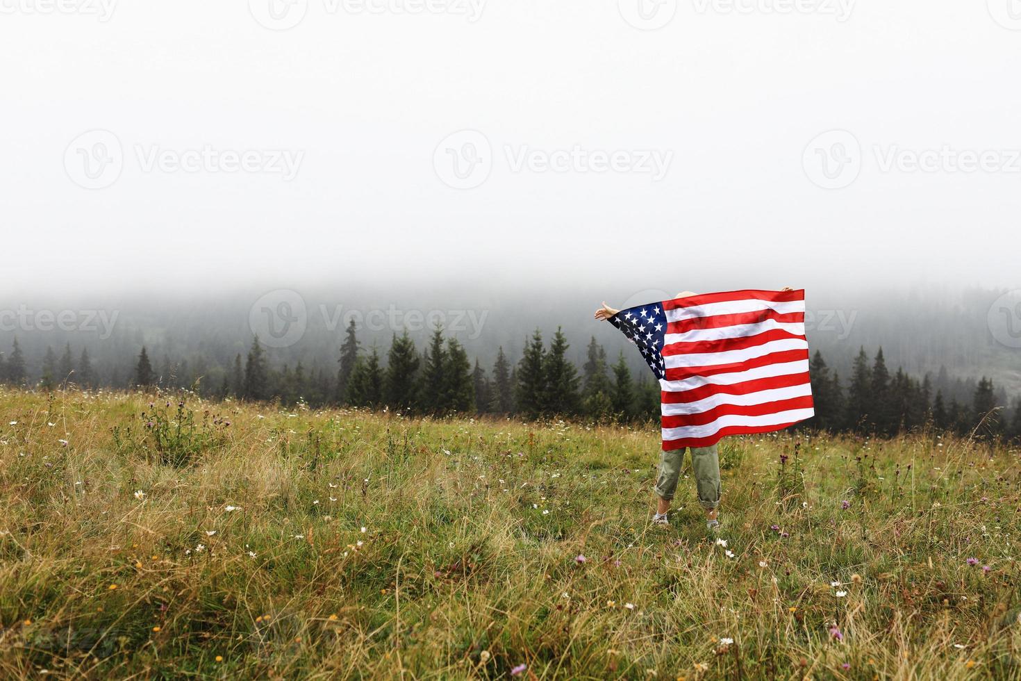 glad bedårande liten flicka ler och viftar med amerikanska flaggan. patriotisk helgdag. glad unge, söt liten barn flicka med amerikanska flaggan. usa firar den 4 juli. självständighetsdagen koncept. foto