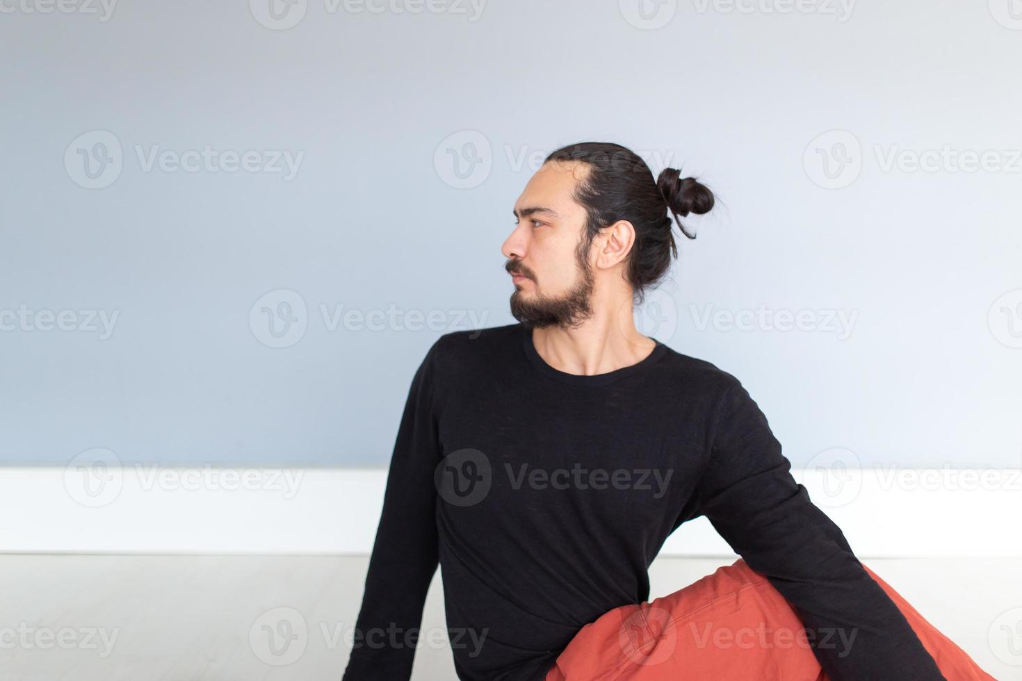 ung kaukasisk långhårig vit man utför yoga i en studio eller ett hus. foto