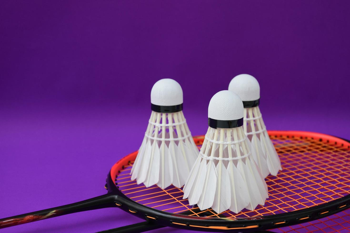 vit krämbadmintonfjäderboll framför badmintonracketar på lila golv på inomhusbadmintonbanan, mjukt och selektivt fokus på fjäderboll, koncept för badmintonsportälskare runt om i världen foto