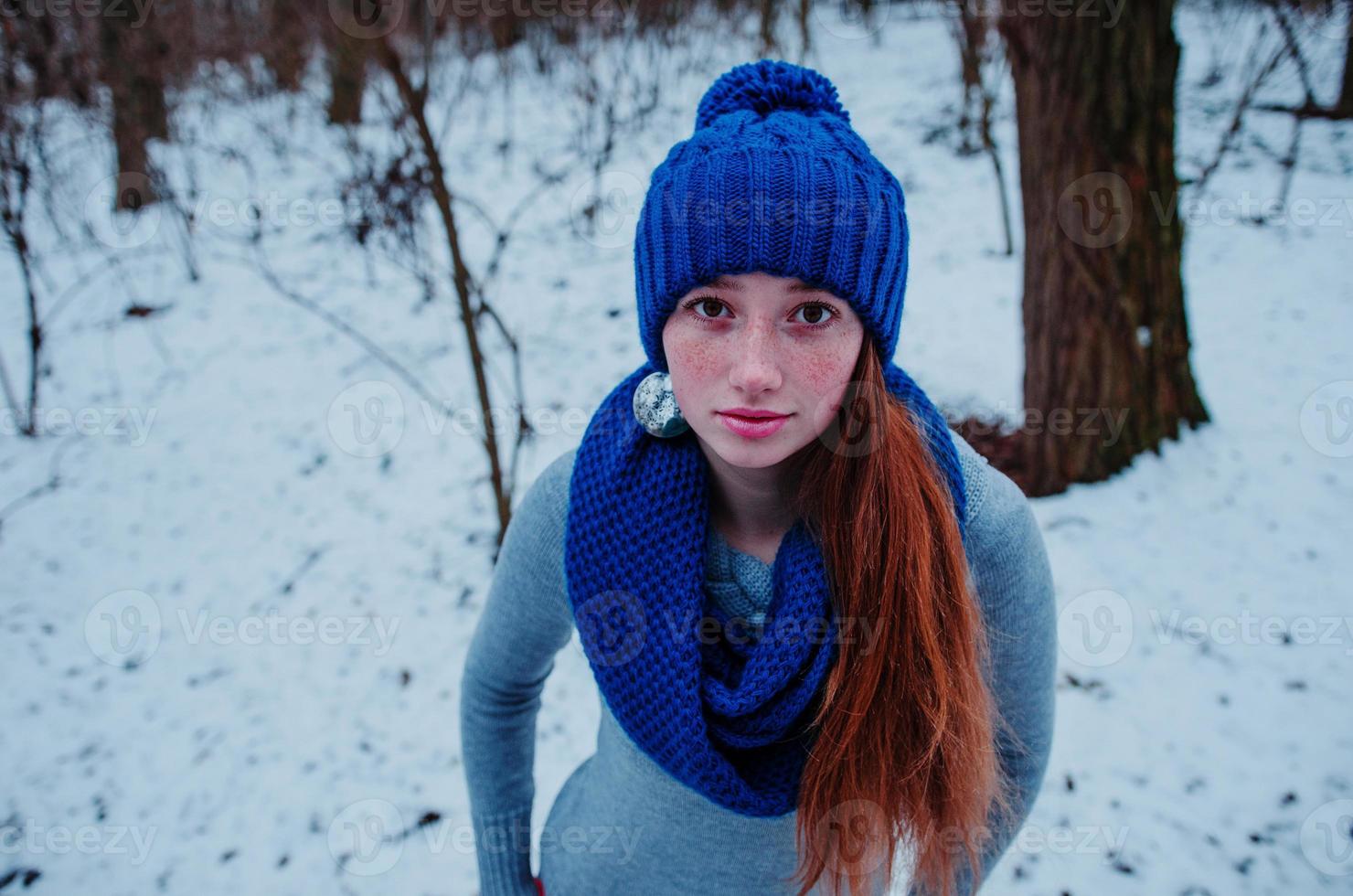 porträtt av ung rött hår flicka med fräknar bär på blå stickad ull mössa och halsduk i vinterdag. foto