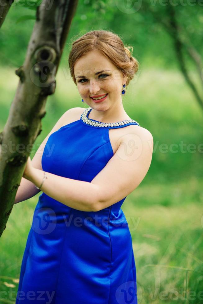 ung överviktig flicka på blå klänning poserade bakgrund vårträdgård. foto