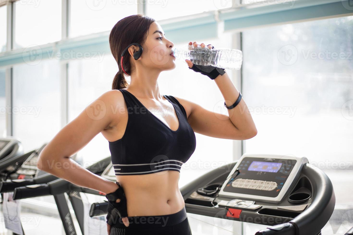 sportig kvinna asien dricker vatten efter övningar i gymmet. fitness - begreppet hälsosamt foto