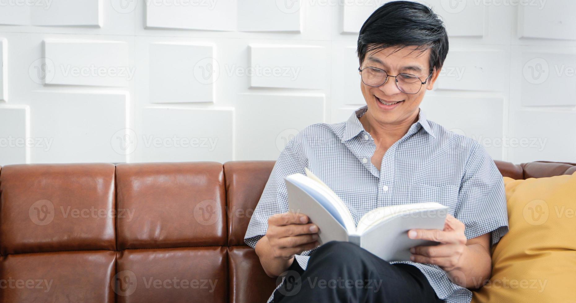 senior asiatisk man läser bok på soffan i vardagsrummet hemma, porträtt av asiatisk äldre man är avkopplande och glädje med att läsa en tidning hemma foto