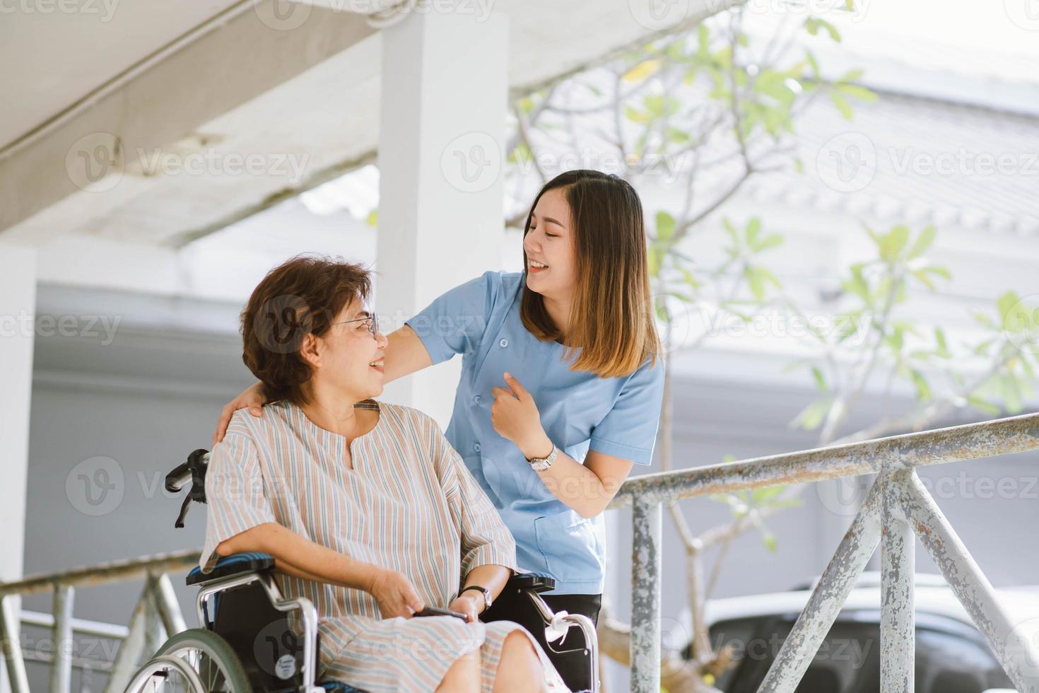 leende sjukgymnast tar hand om den glada äldre patienten i rullstol foto