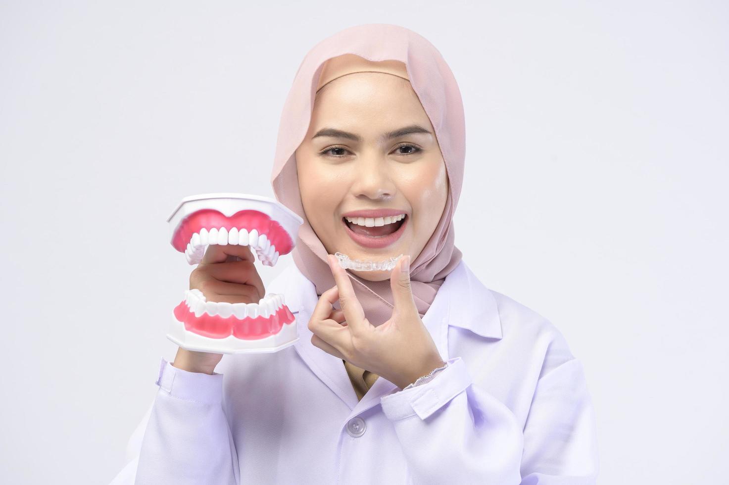 muslimsk kvinnlig tandläkare håller invisalign hängslen över vit bakgrund studio, tandvård och ortodontisk koncept. foto