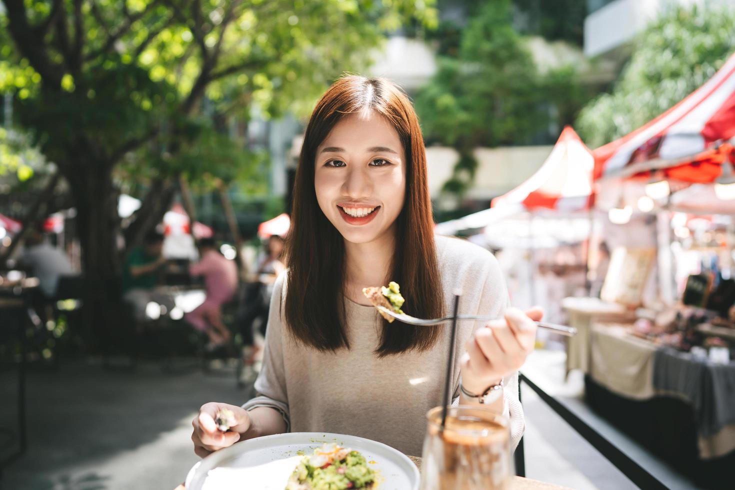 ung vuxen asiatisk kvinna äter lunchmat på restaurang utomhus på helgdagen foto