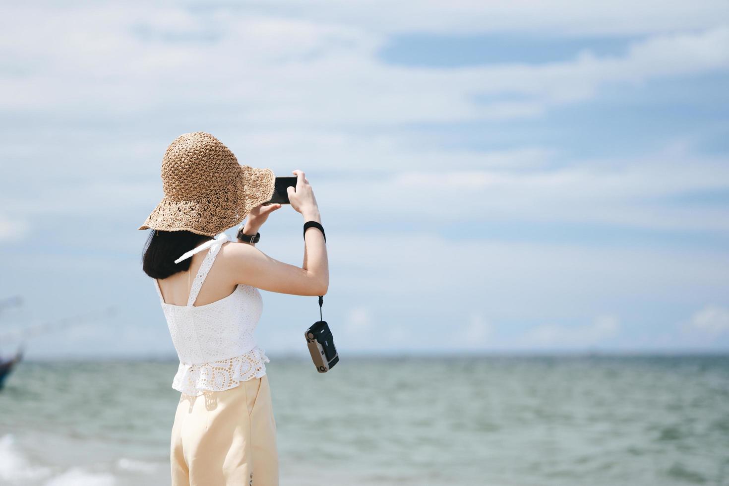 asiatisk kvinna koppla av sommaren utomhus på stranden ta ett foto med smartphone och filmkamera