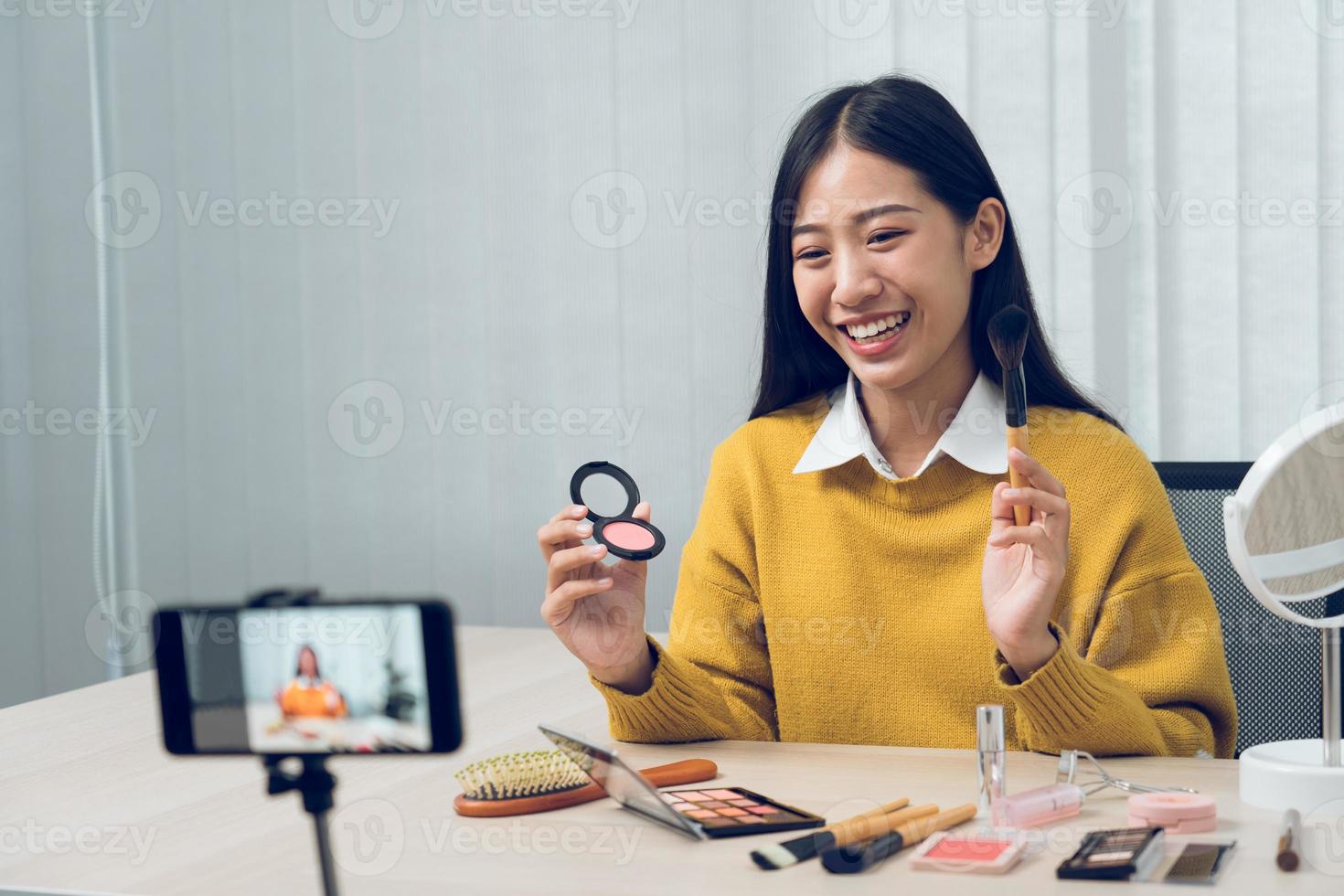 ung asiatisk kvinna som vloggar sig själv om skönhetsprodukter med att göra en video för sin blogg om kosmetika med hjälp av telefonkamera hemma. foto