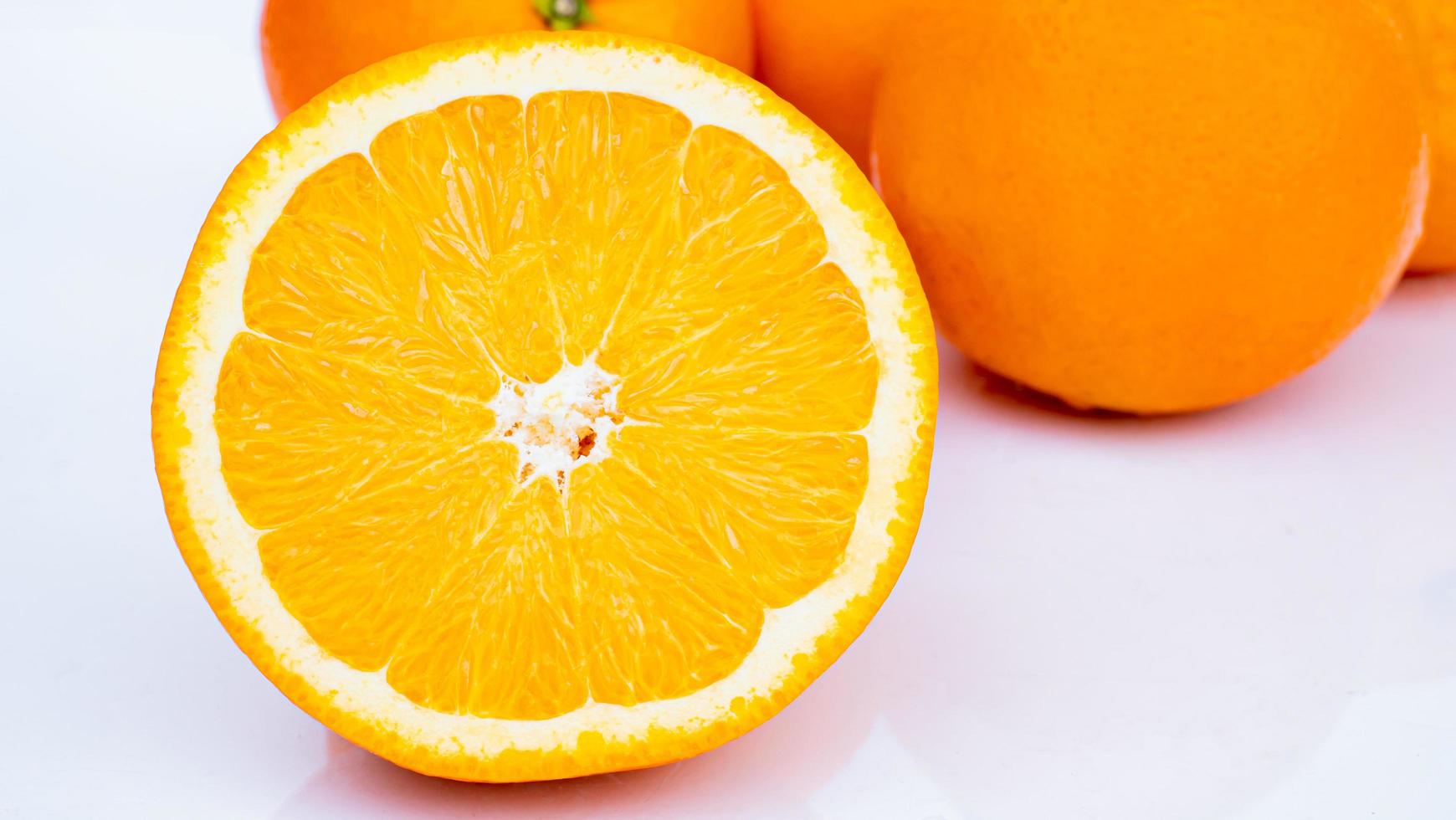 halvera och skiva en mogen apelsin med gyllengult skal. massor på vit bakgrund med skuggor och reflektioner foto